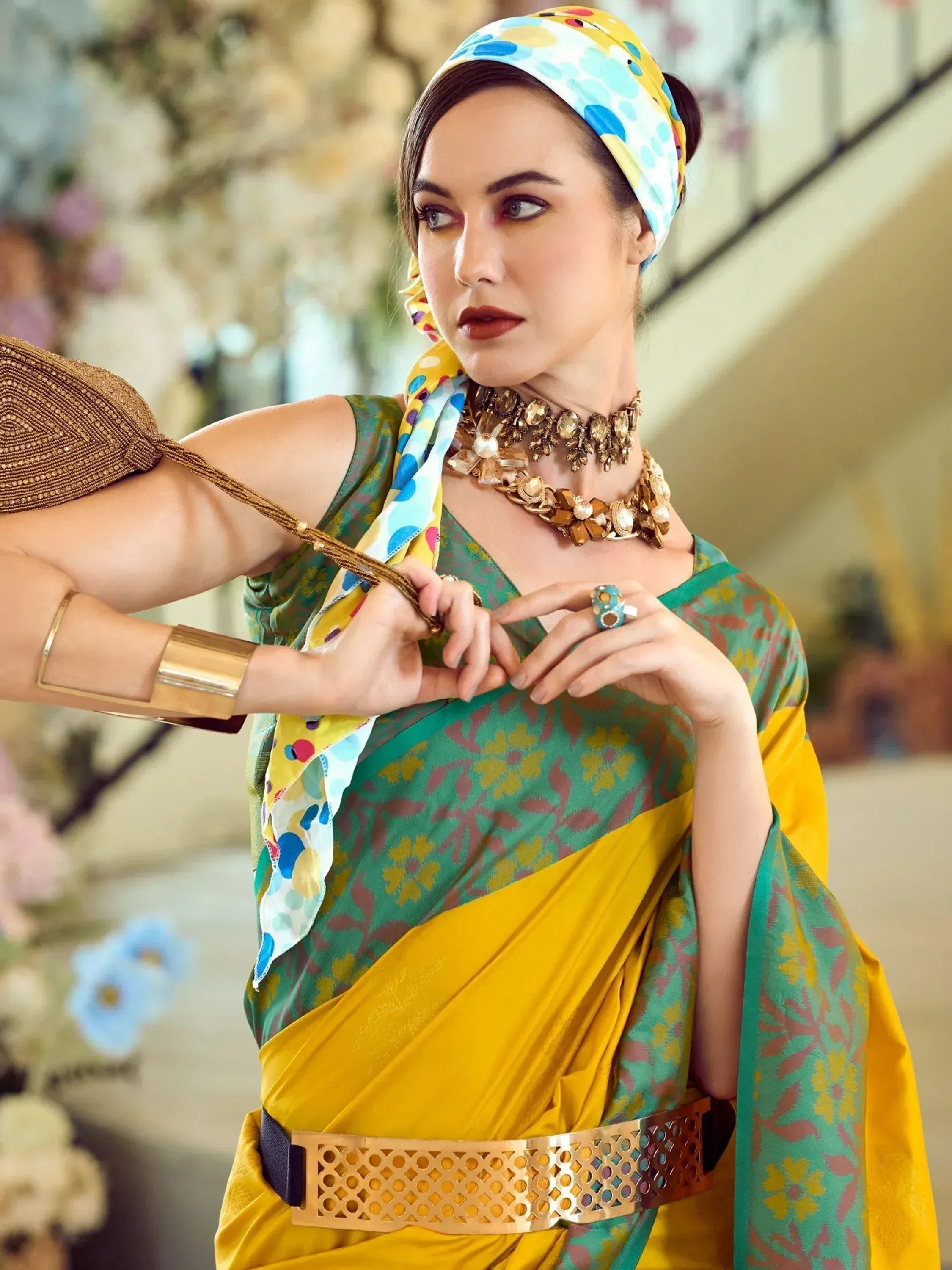 Woman in vibrant green and yellow floral saree with colorful headscarf, statement jewelry, and gold belt