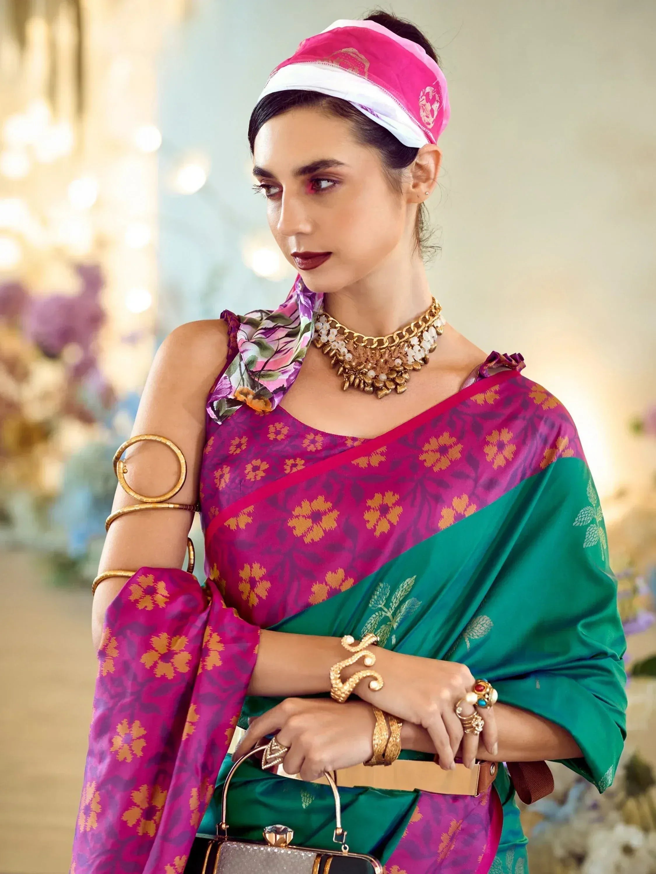 Woman in vibrant pink and green floral saree with gold jewelry and headscarf, styled for ethnic occasions