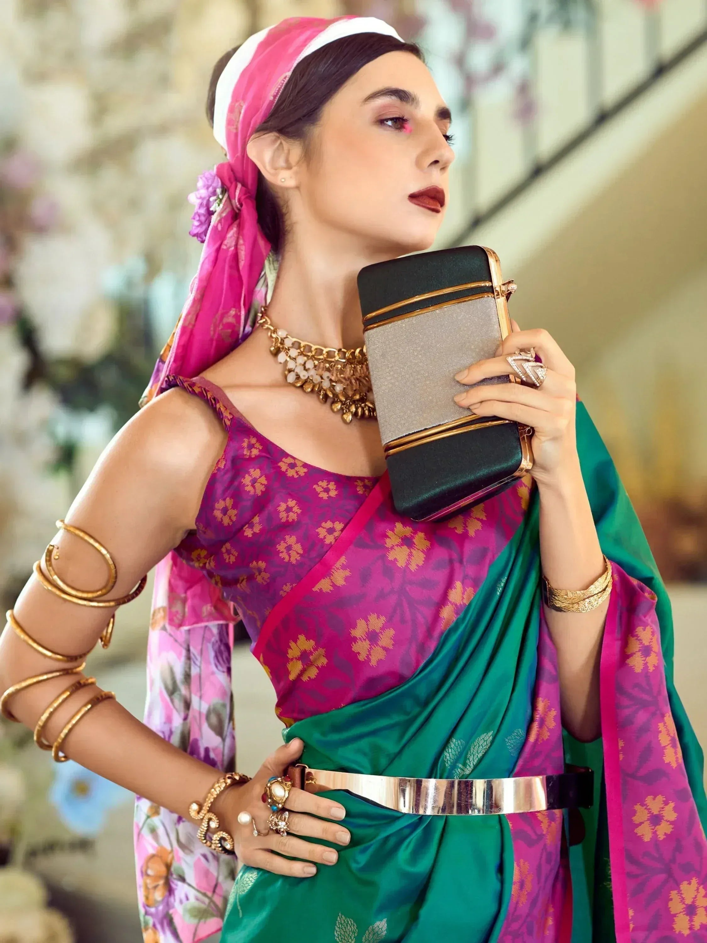 Woman in vibrant purple and green saree with gold jewelry, holding clutch, styled for ethnic occasions