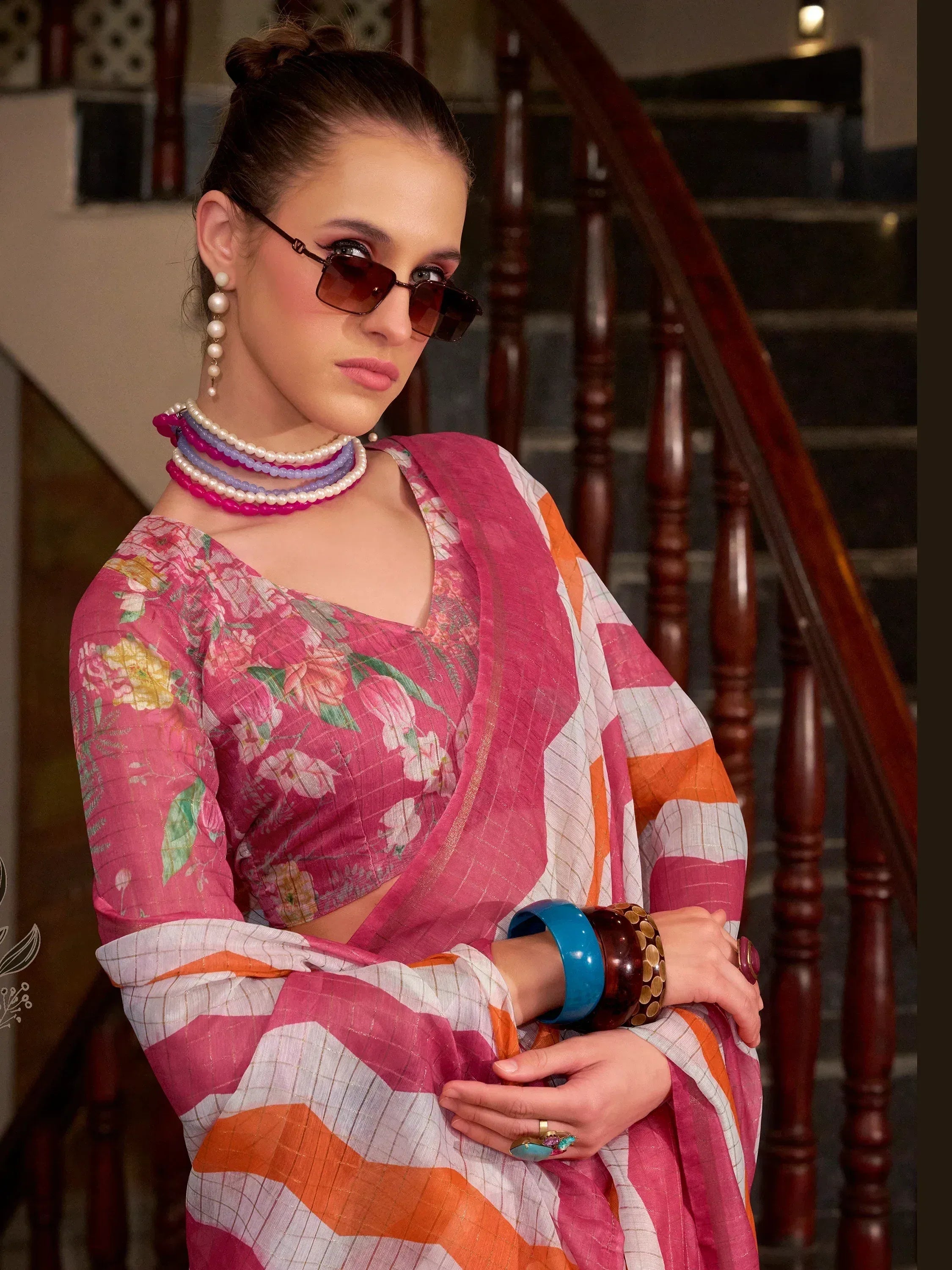 Stylish woman in floral pink saree with orange stripes, accessorized with pearl necklaces and sunglasses