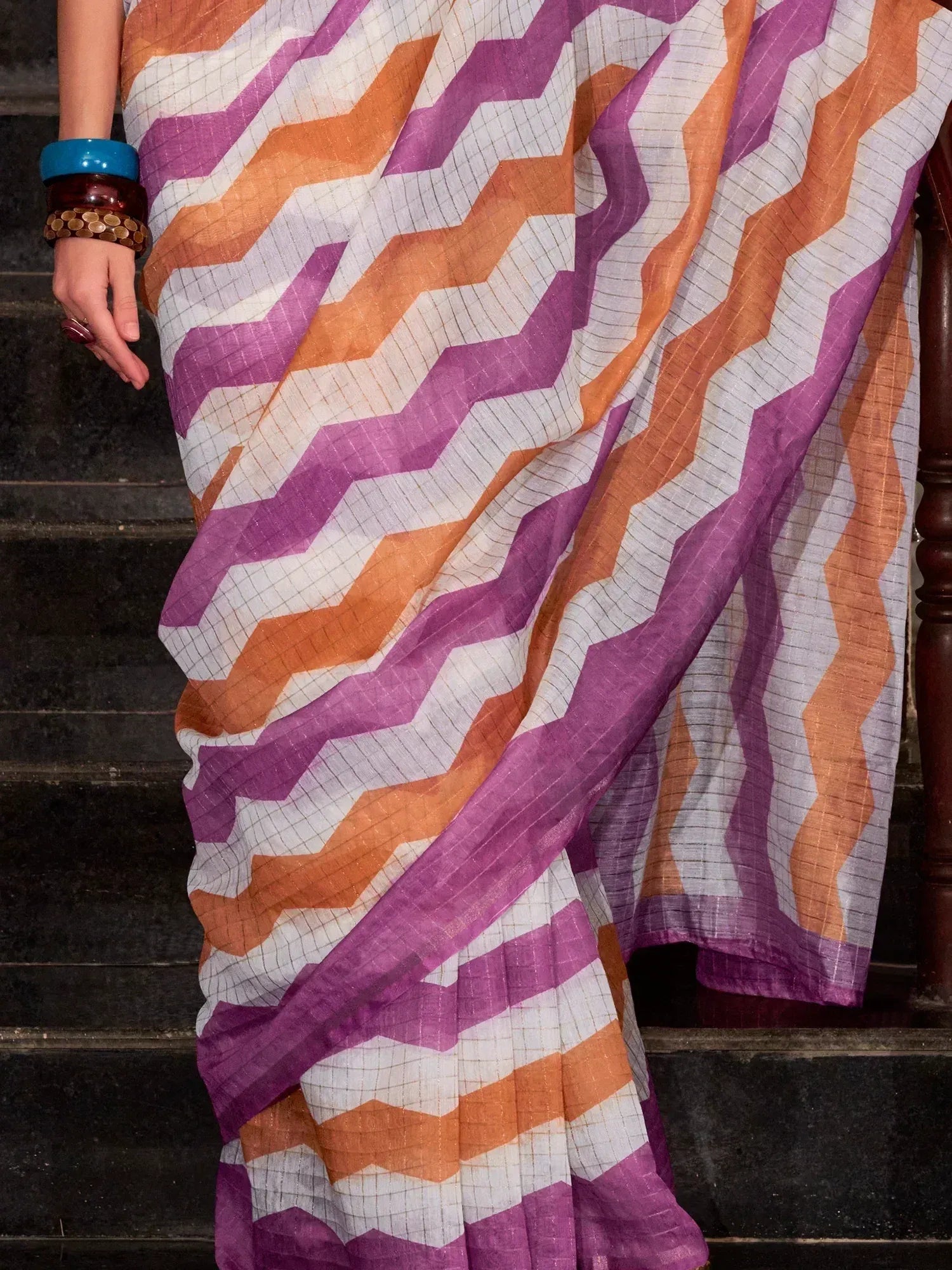 Vibrant zigzag patterned saree in purple, orange, and white, styled with colorful bangles.