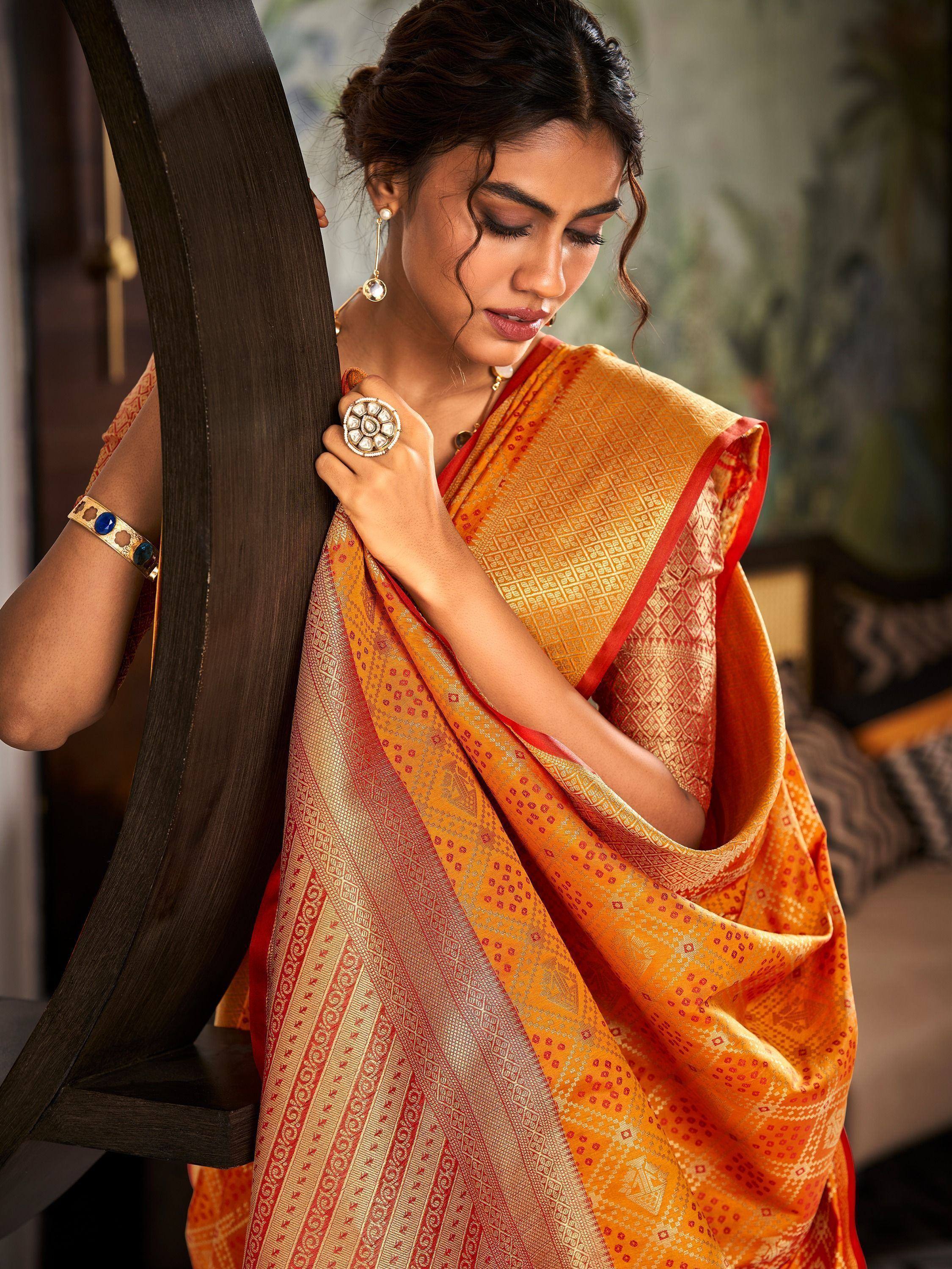 Woman in vibrant orange and red ethnic saree with gold patterns, styled with traditional jewelry