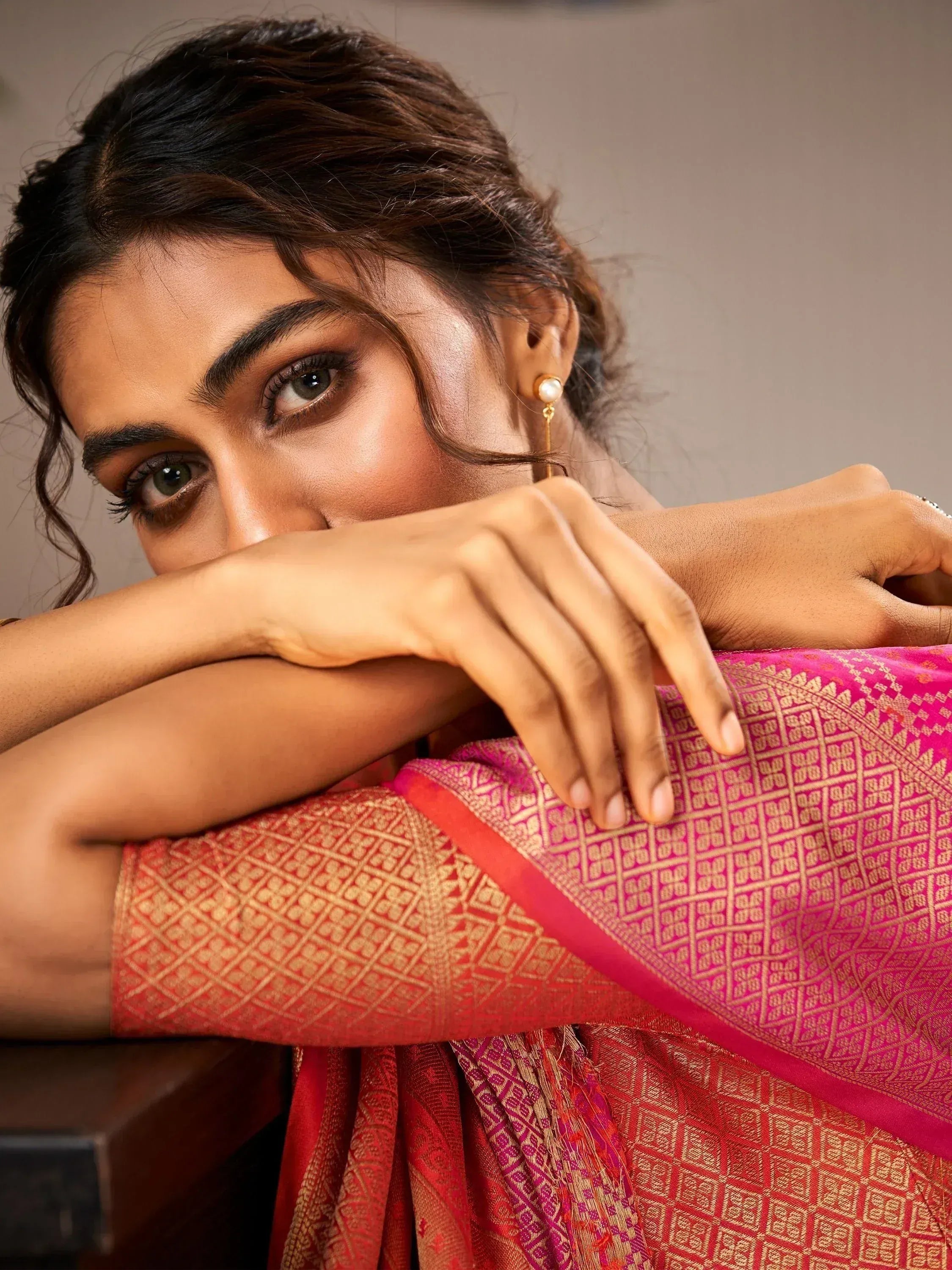 Woman in vibrant pink and red ethnic saree with gold geometric patterns, styled with pearl earrings.
