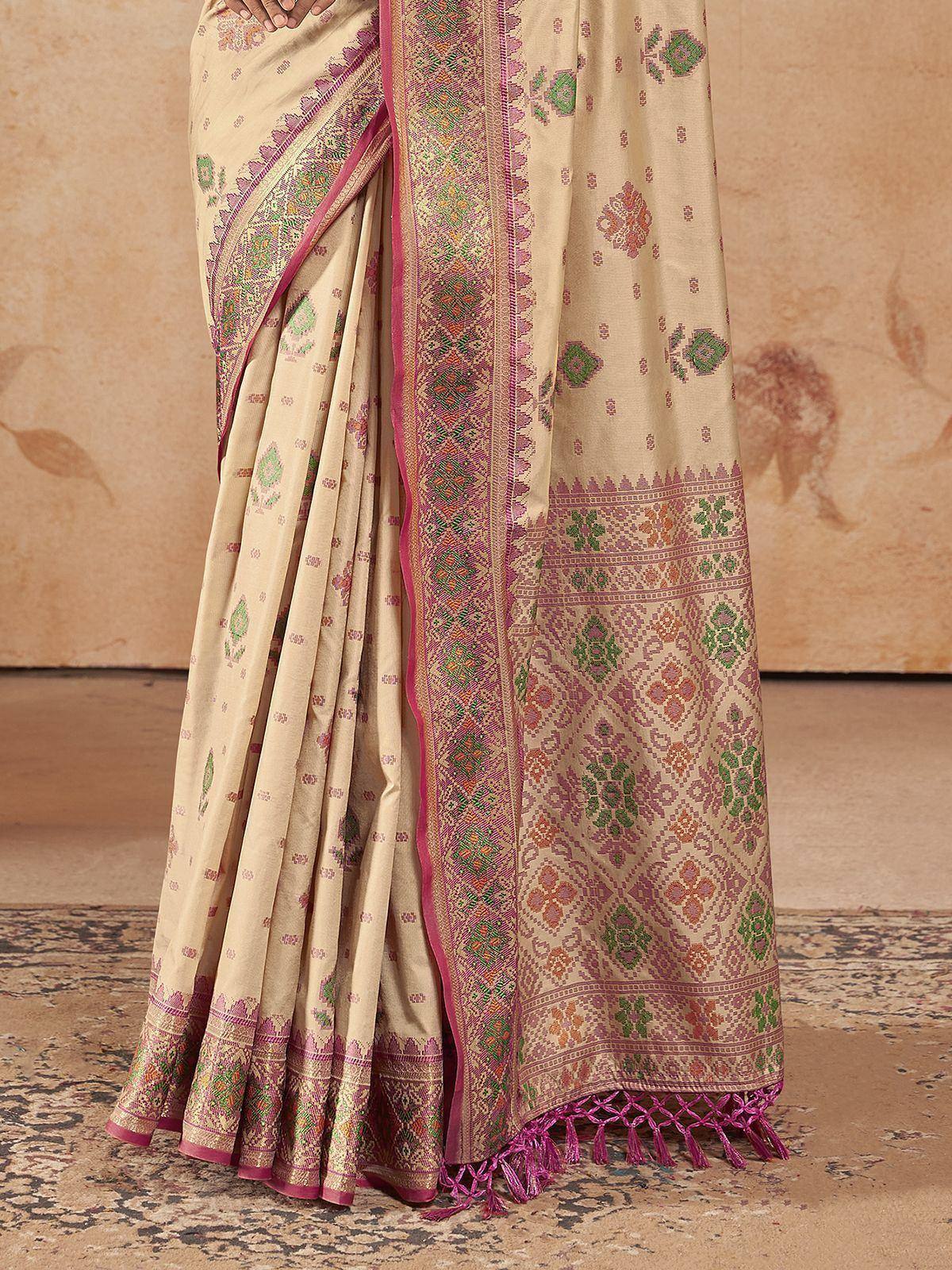 Beige saree with pink and green floral motifs, intricate border, and tassels, ideal for ethnic occasions.
