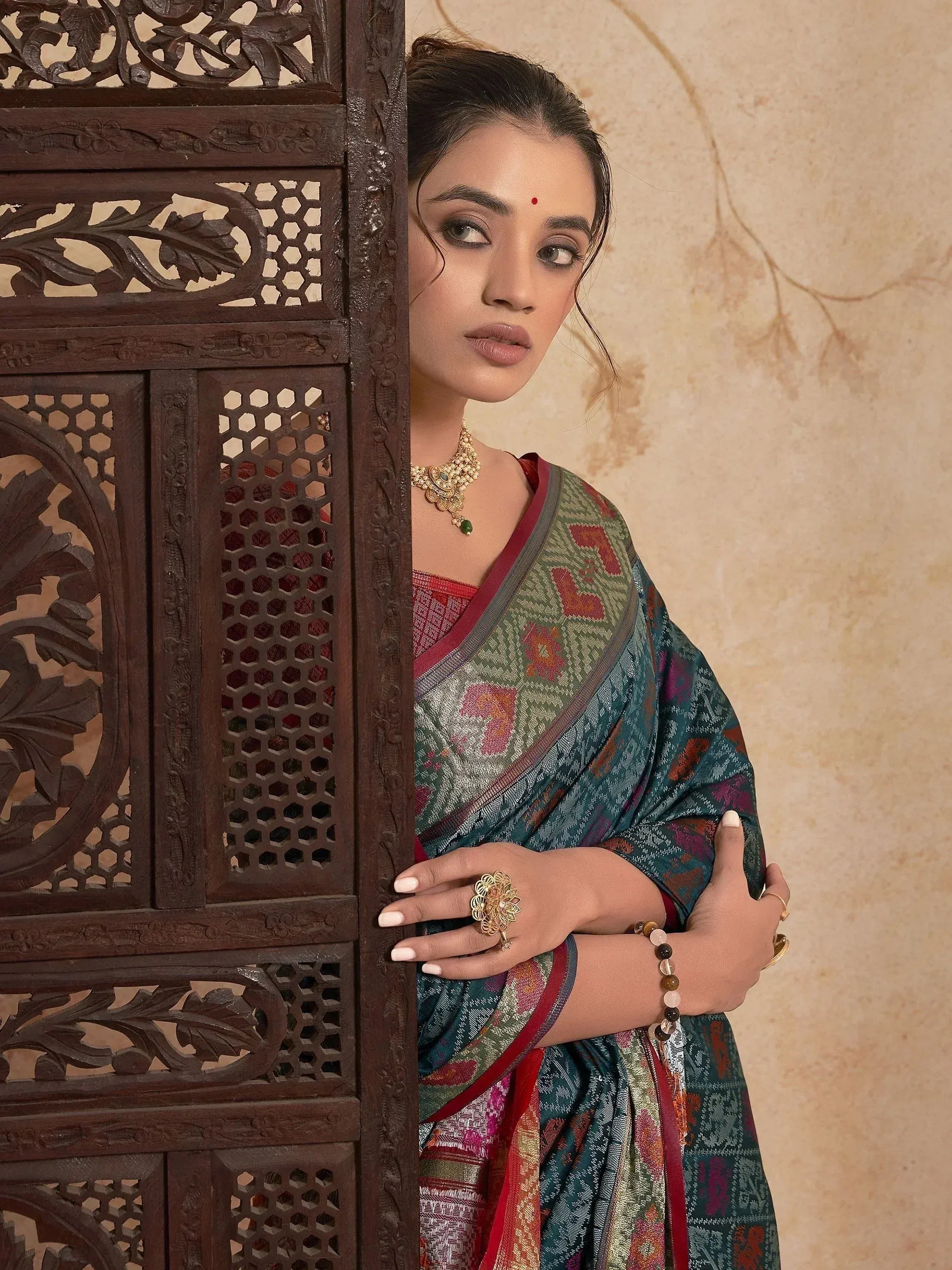 Woman in colorful ethnic saree with gold jewelry peeking from carved wooden panel
