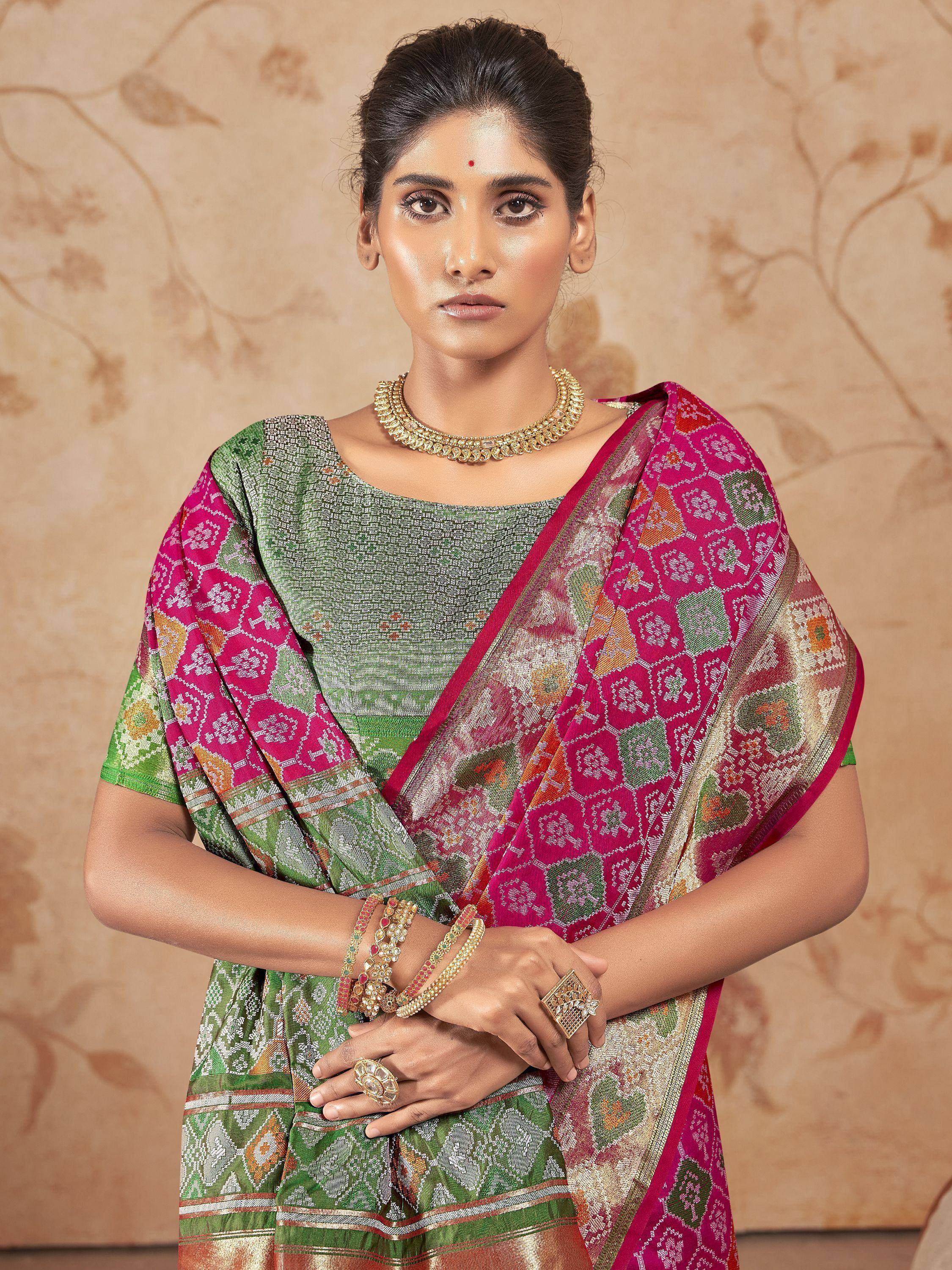 Woman in vibrant pink and green ethnic saree with intricate patterns, paired with gold jewelry