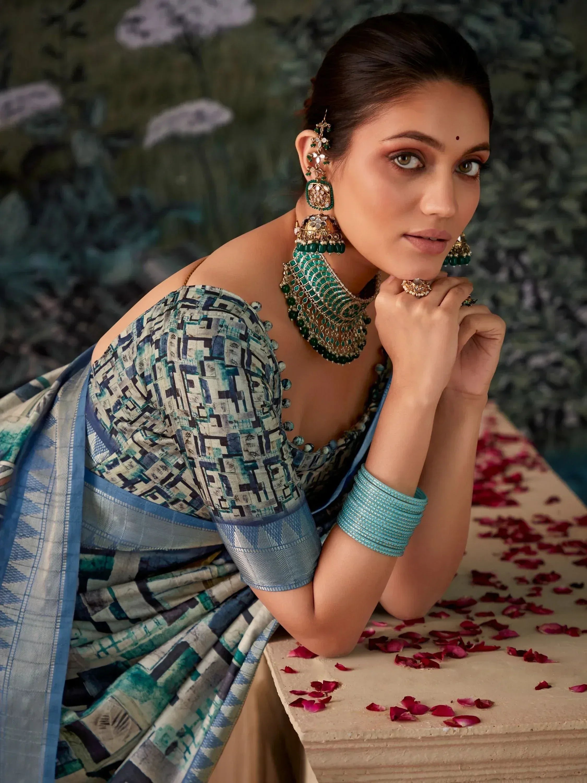 Woman in blue geometric print saree with green jewelry, rose petals, ethnic wear