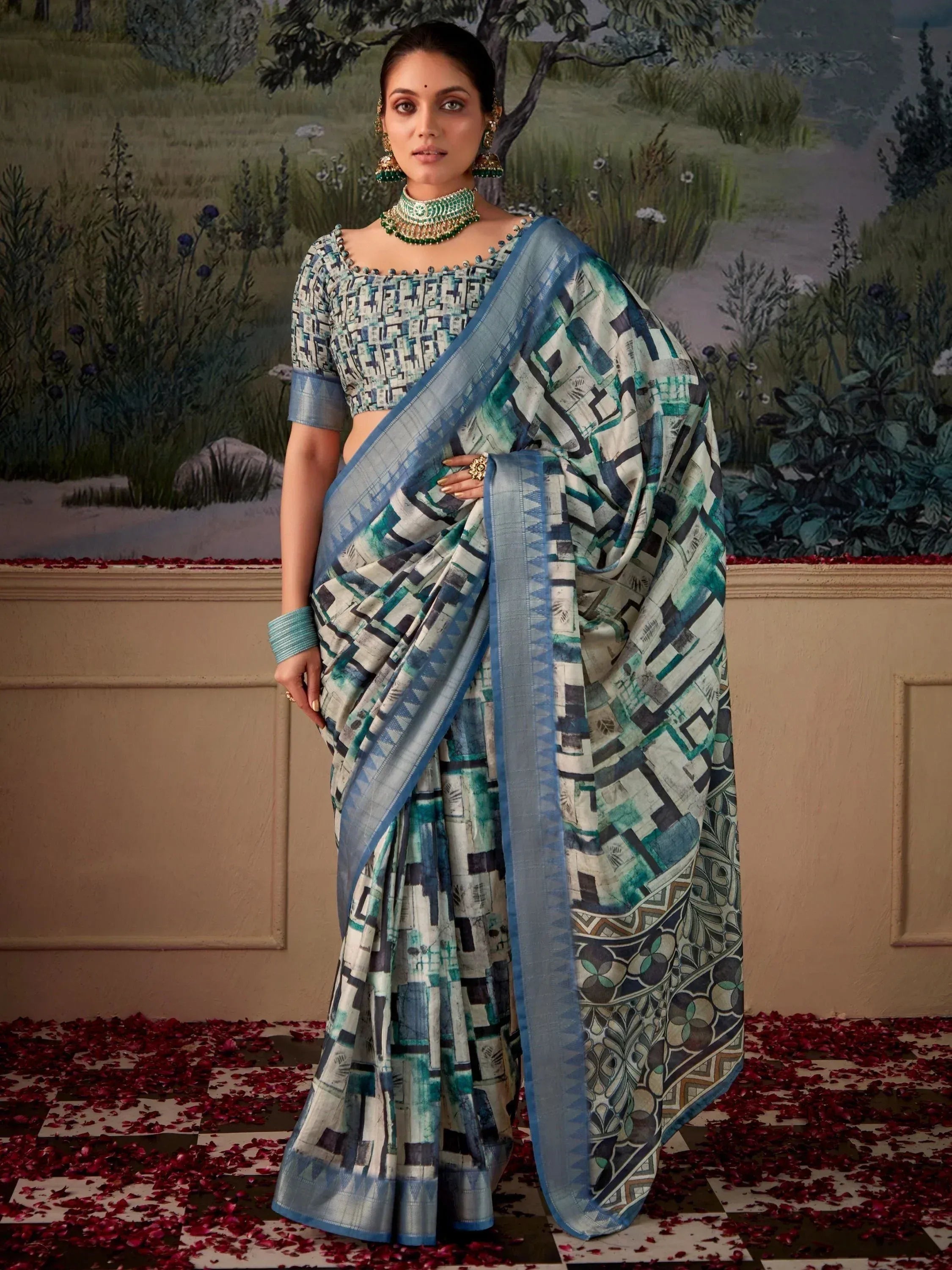 Woman in blue and green printed saree with matching blouse, ethnic jewelry, standing on rose petals