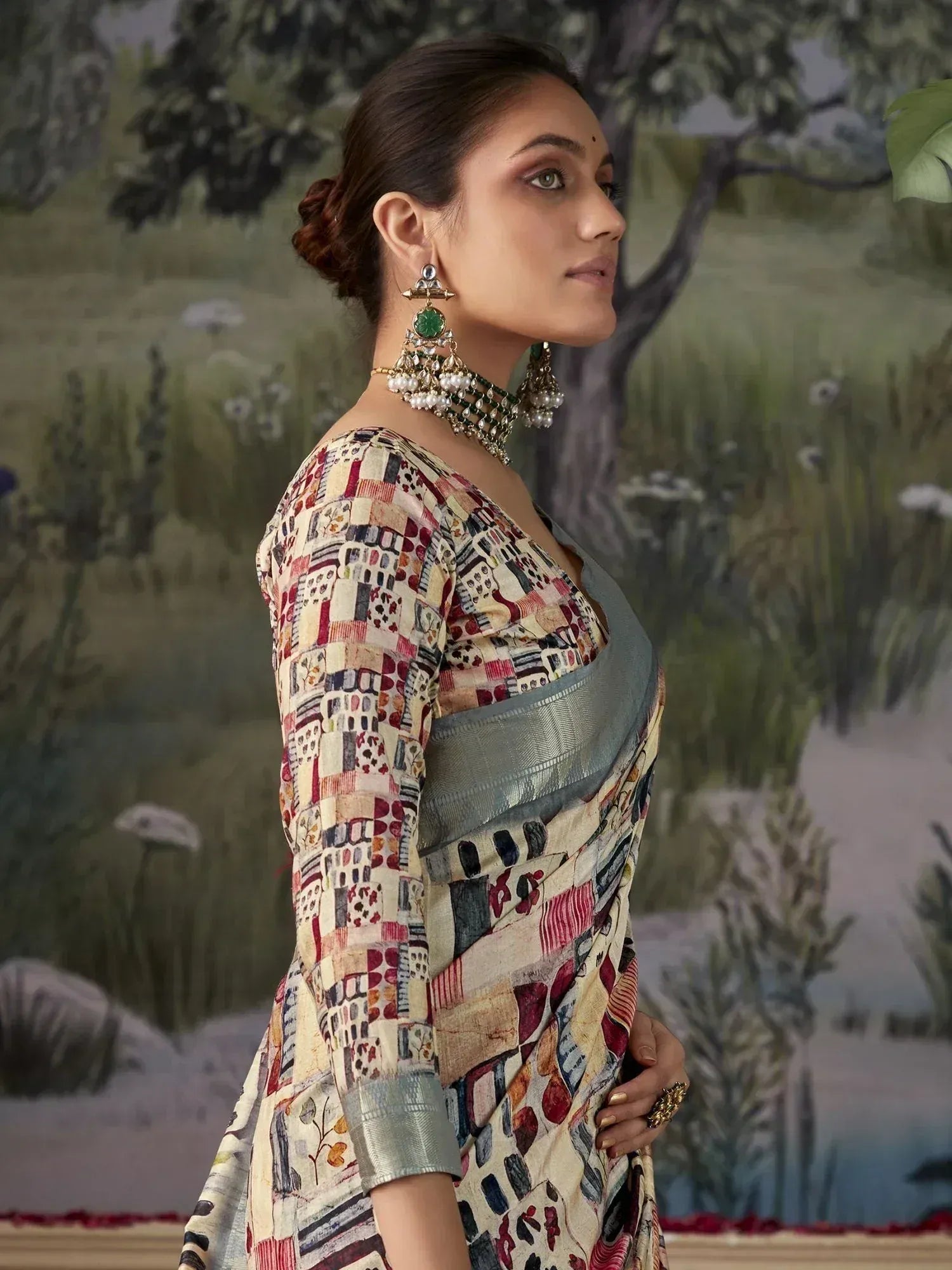 Woman in printed ethnic saree with green border, traditional jewelry, and side profile pose