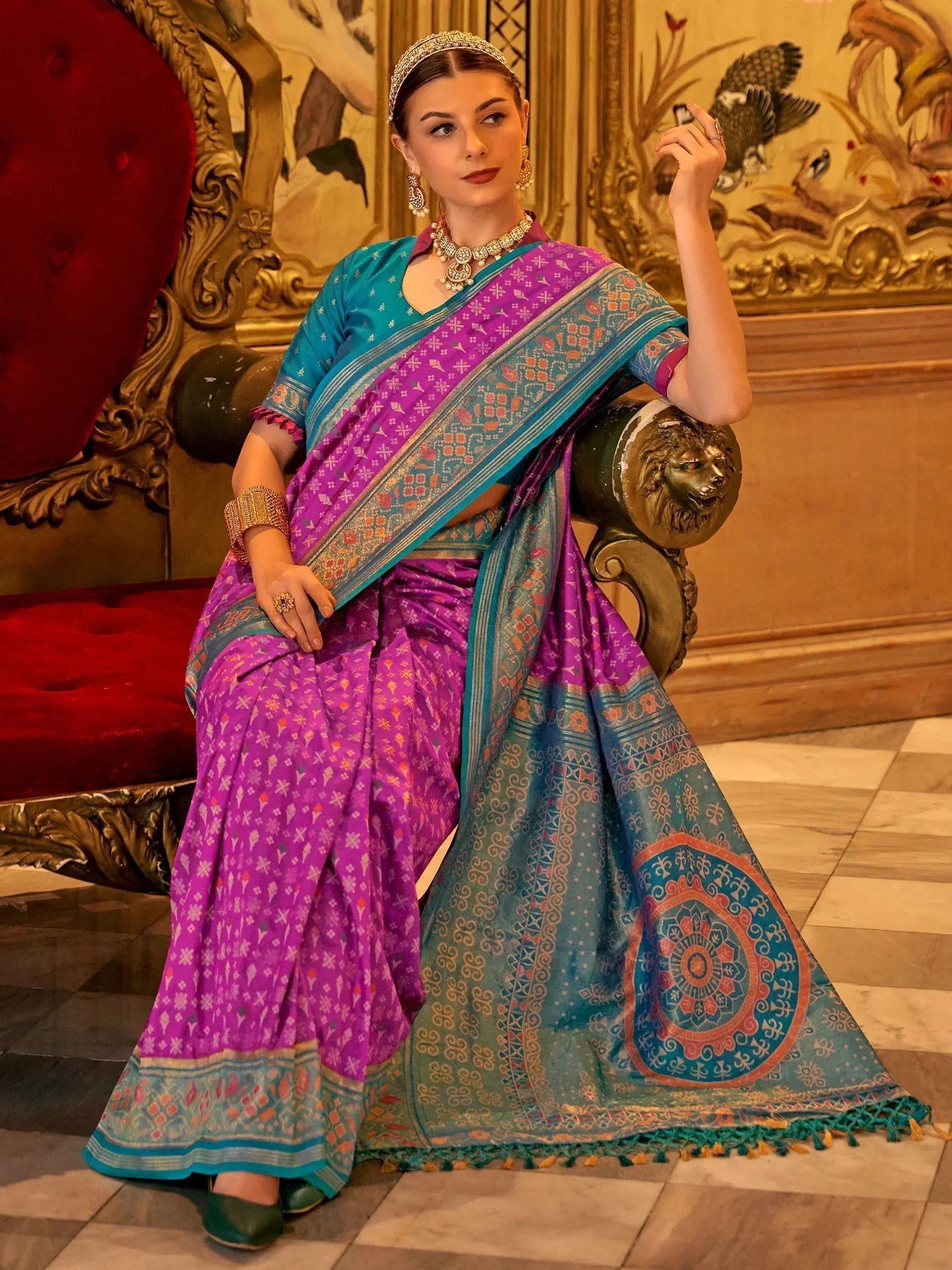 Woman in vibrant purple and teal ethnic saree with intricate patterns, traditional jewelry, seated on ornate chair