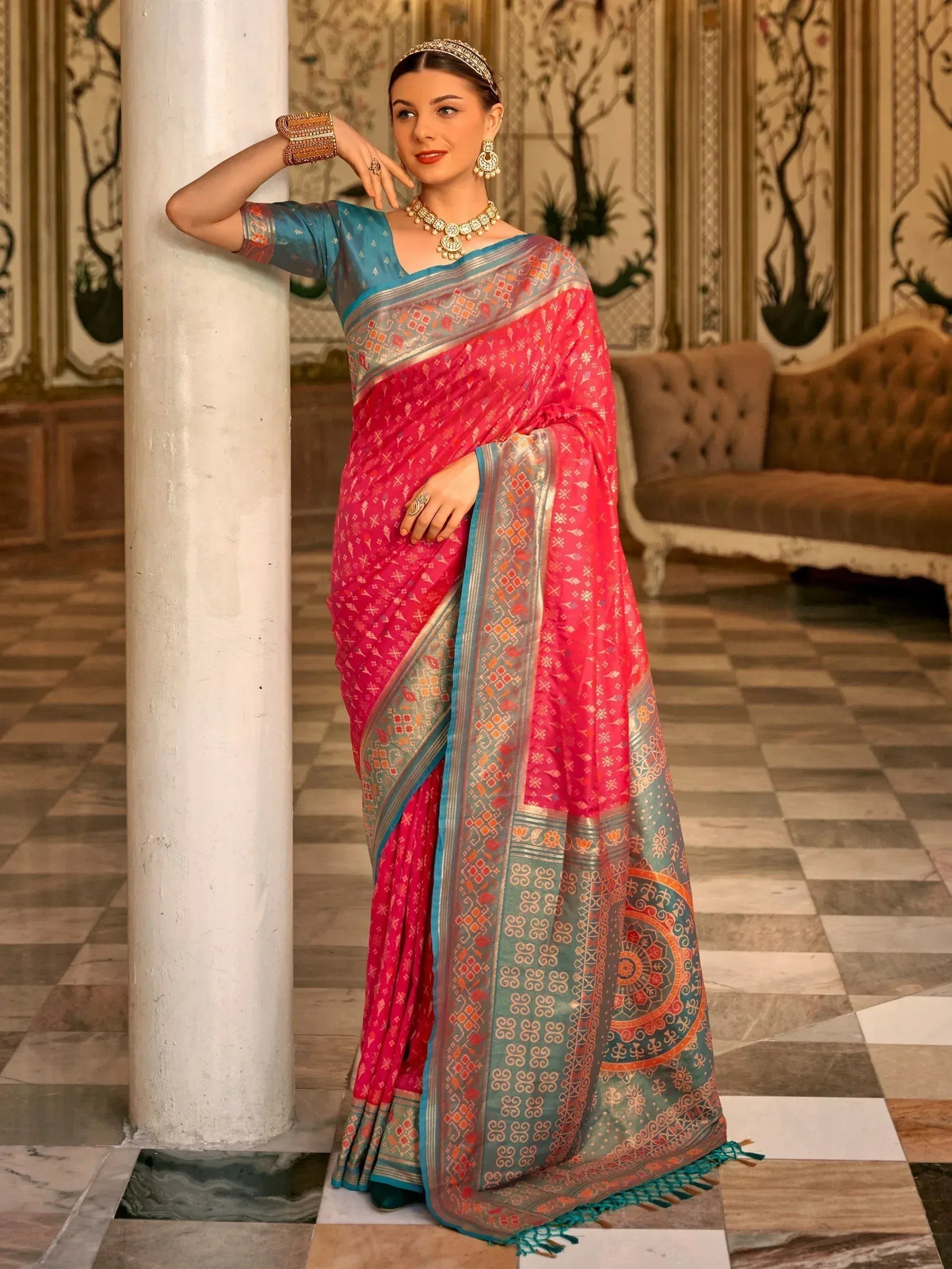 Woman in vibrant pink and blue designer saree with intricate patterns, traditional jewelry, and ethnic styling