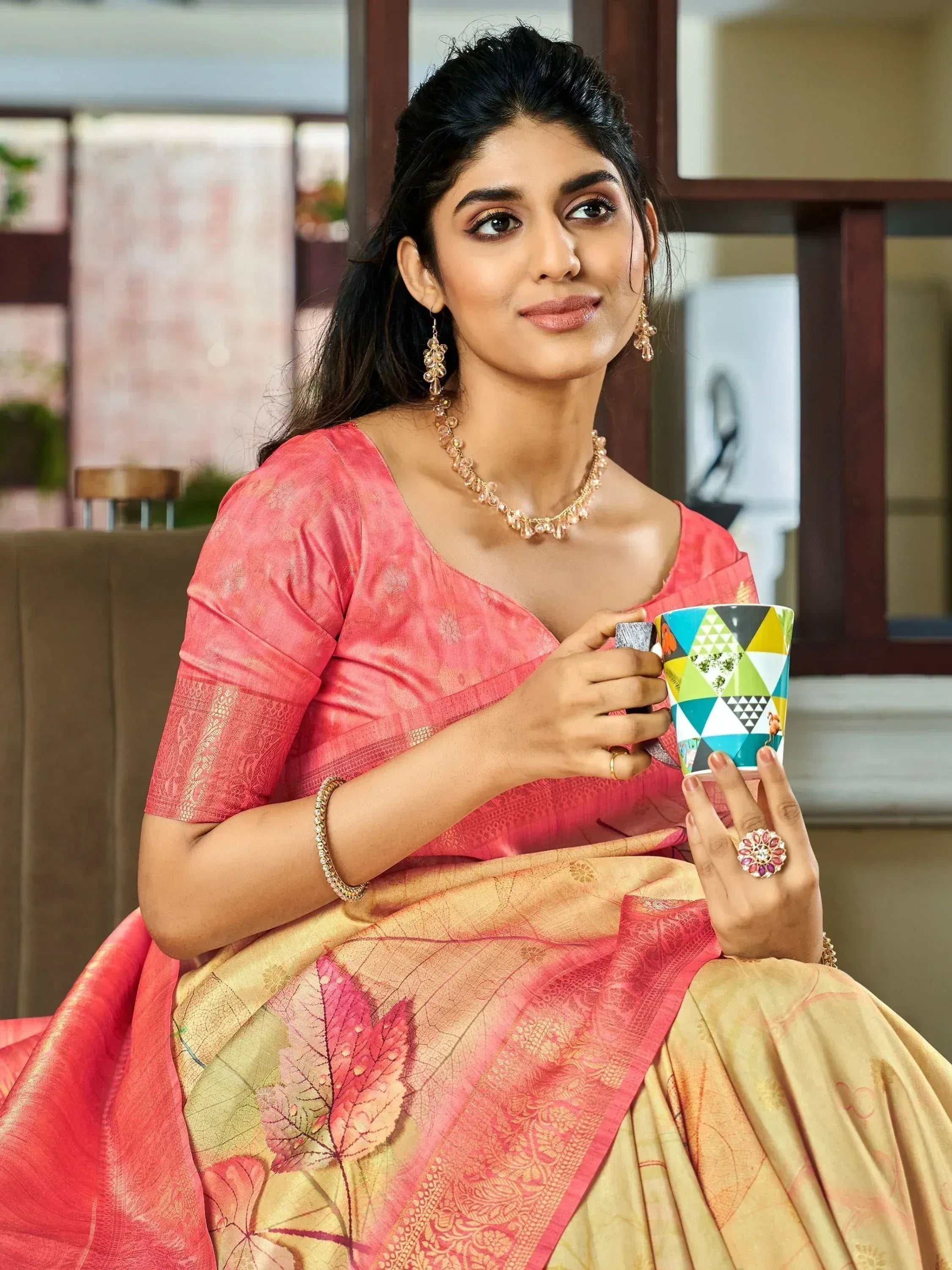 Woman in pink and gold ethnic saree holding colorful mug, adorned with jewelry
