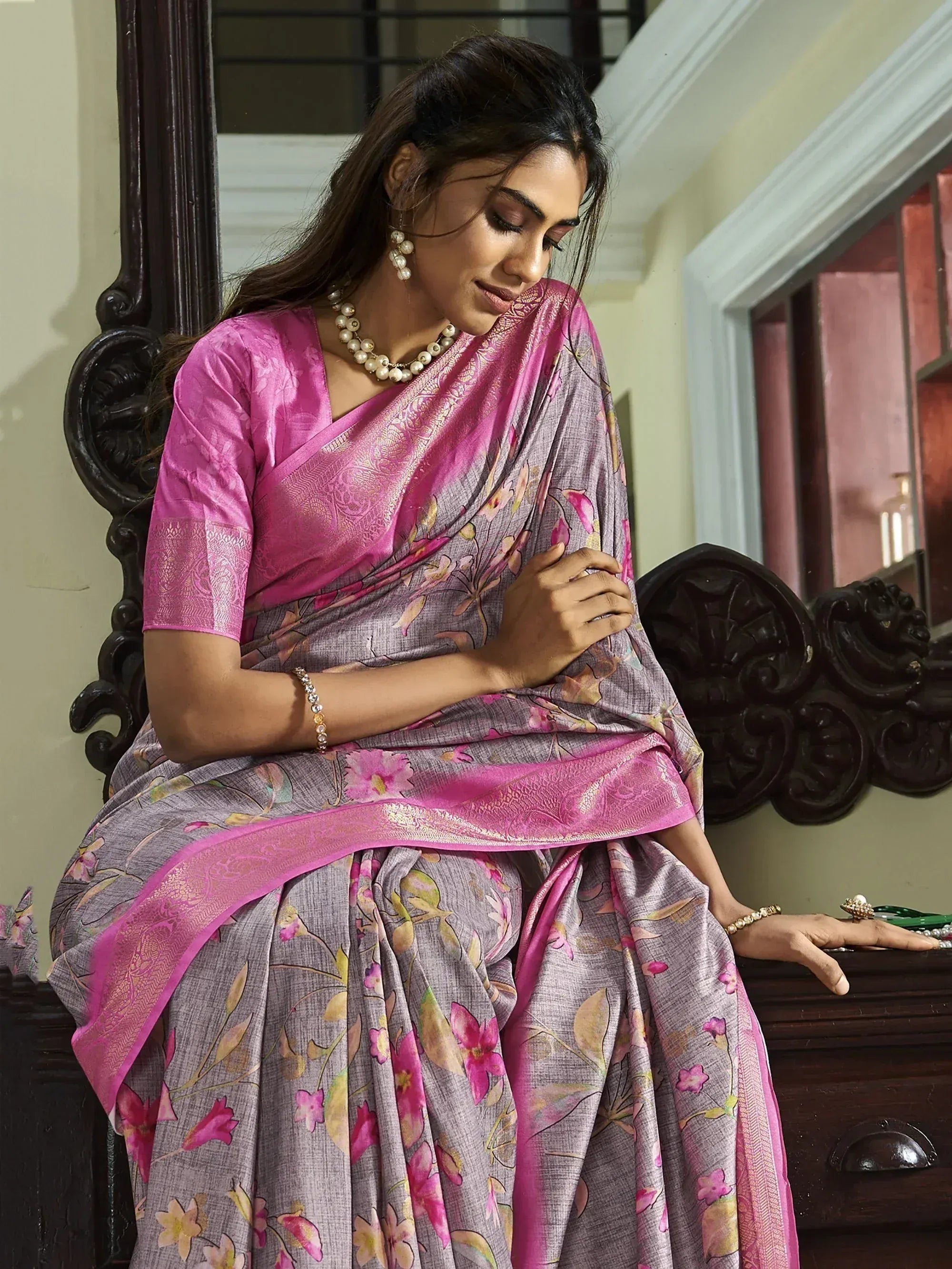 Woman in grey floral saree with pink border and matching blouse, styled with pearl jewelry