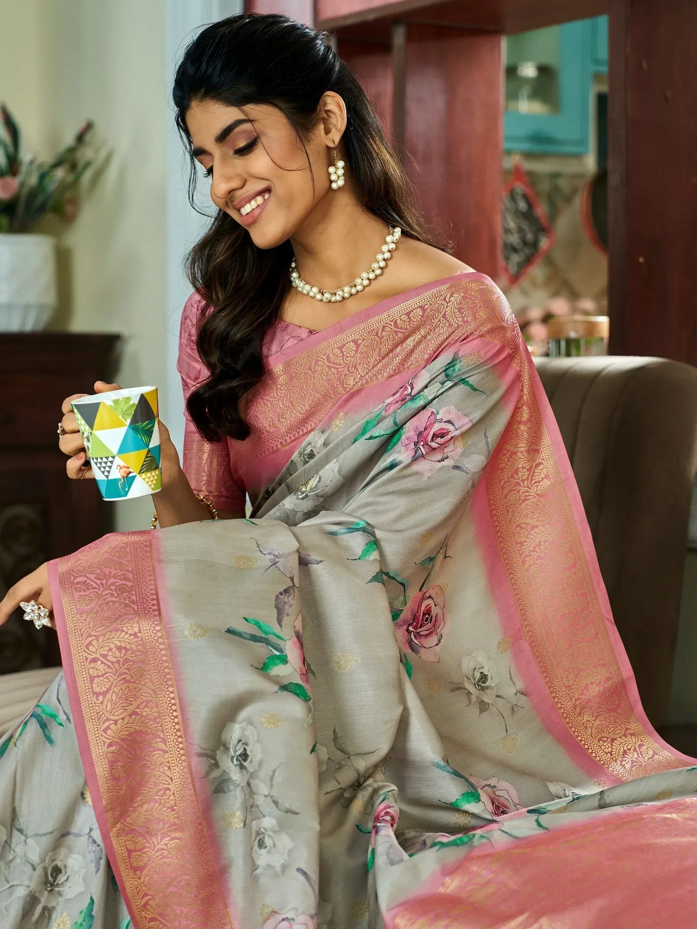 Woman in floral print saree with pink border, gold embroidery, holding mug, ethnic wear