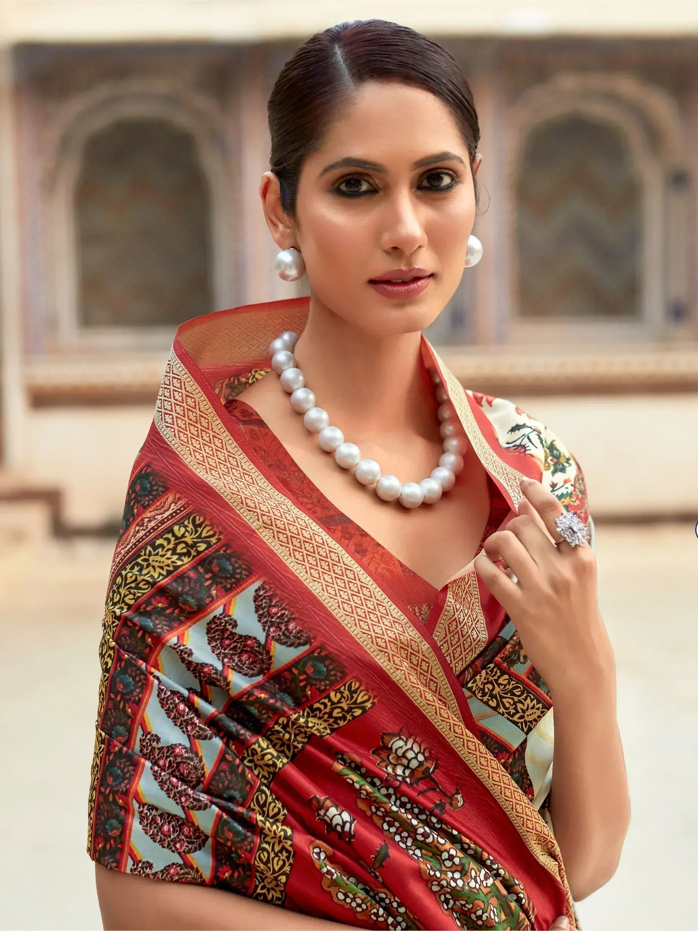 Elegant woman in red floral saree with gold border, pearl jewelry, and traditional Indian attire.