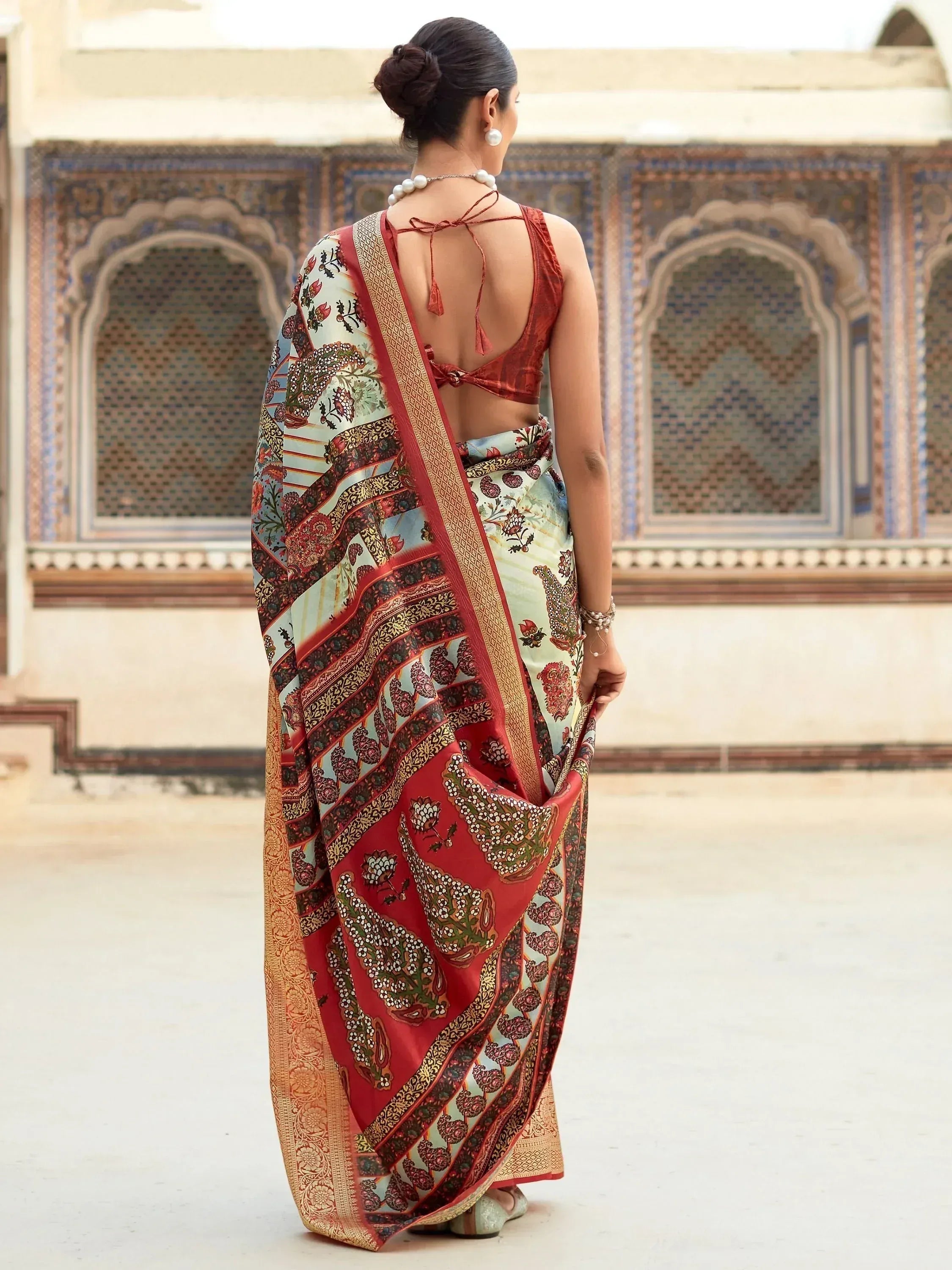 Elegant Indian saree with floral and paisley patterns, paired with a red blouse, showcased against traditional architecture.