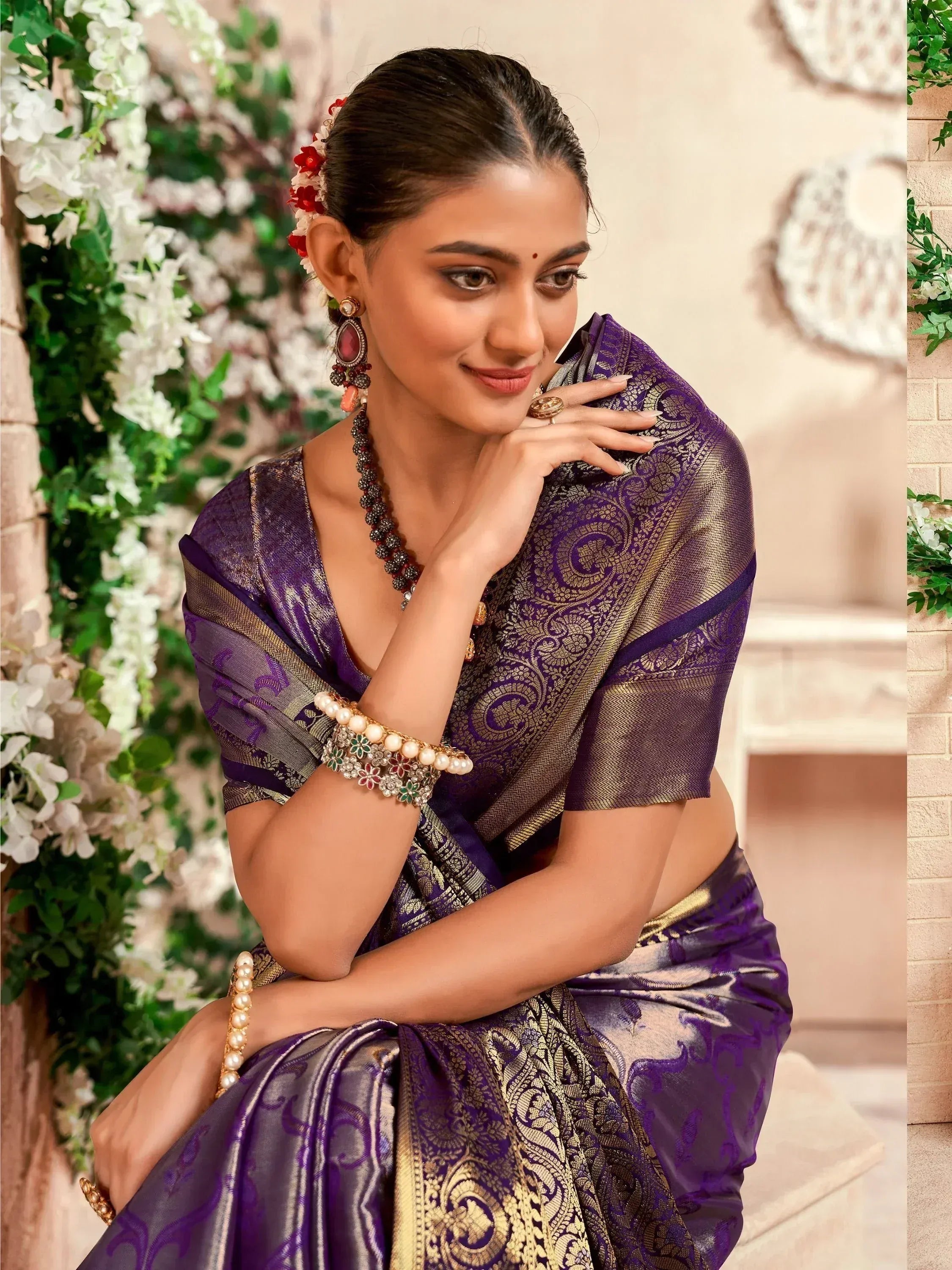 Elegant woman in purple and gold designer saree with floral hair accessories, perfect for Indian ethnic occasions.