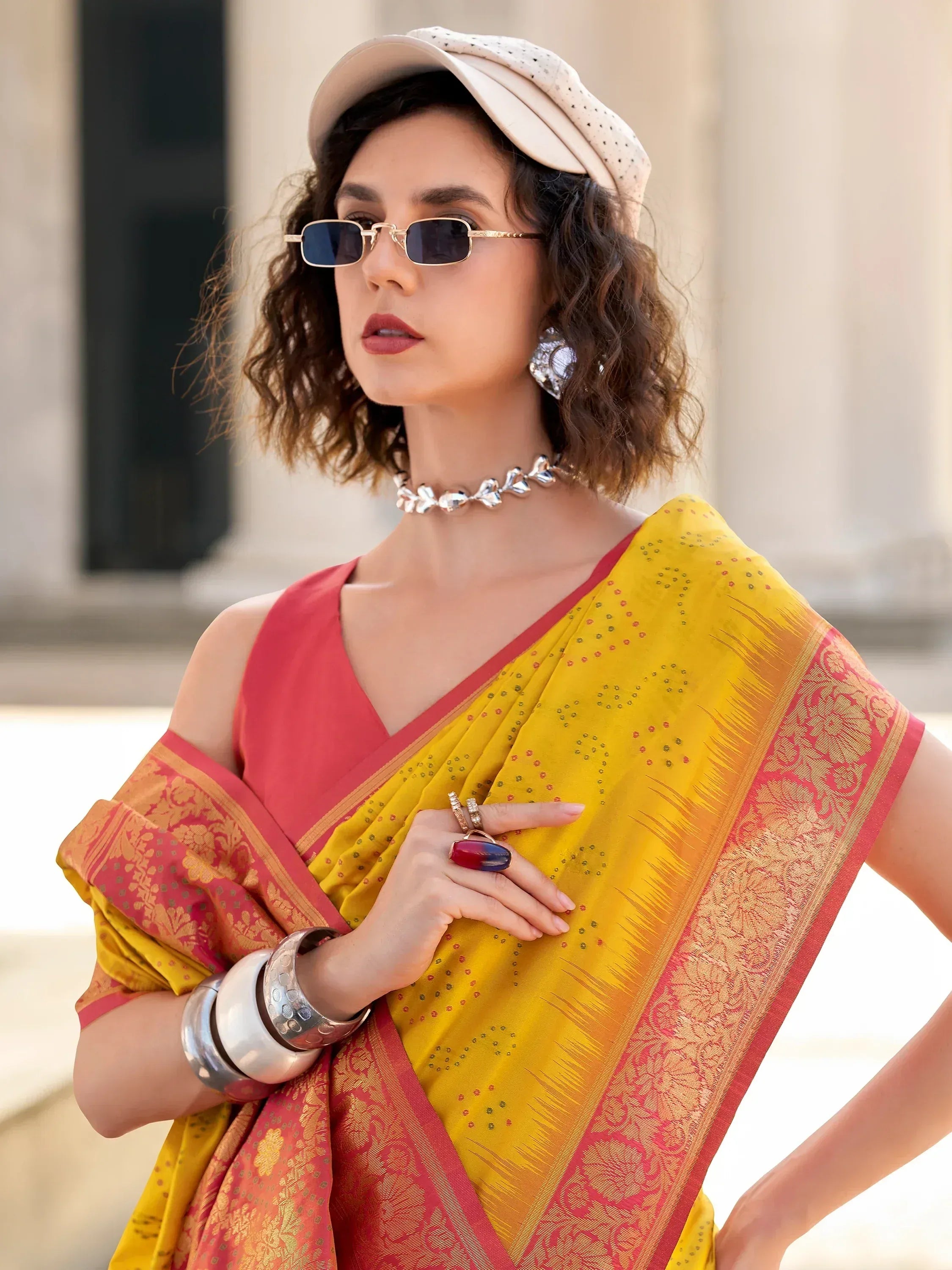 Yellow and pink ethnic saree with gold border, paired with modern sunglasses and cap for stylish Indian wear