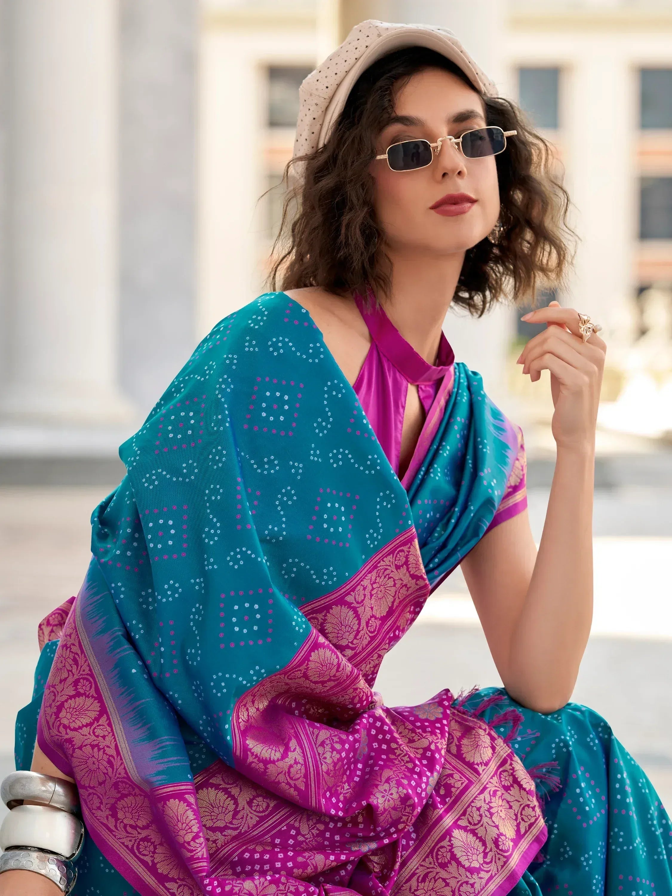 Stylish woman in teal and magenta ethnic saree with gold border, modern sunglasses, and cap