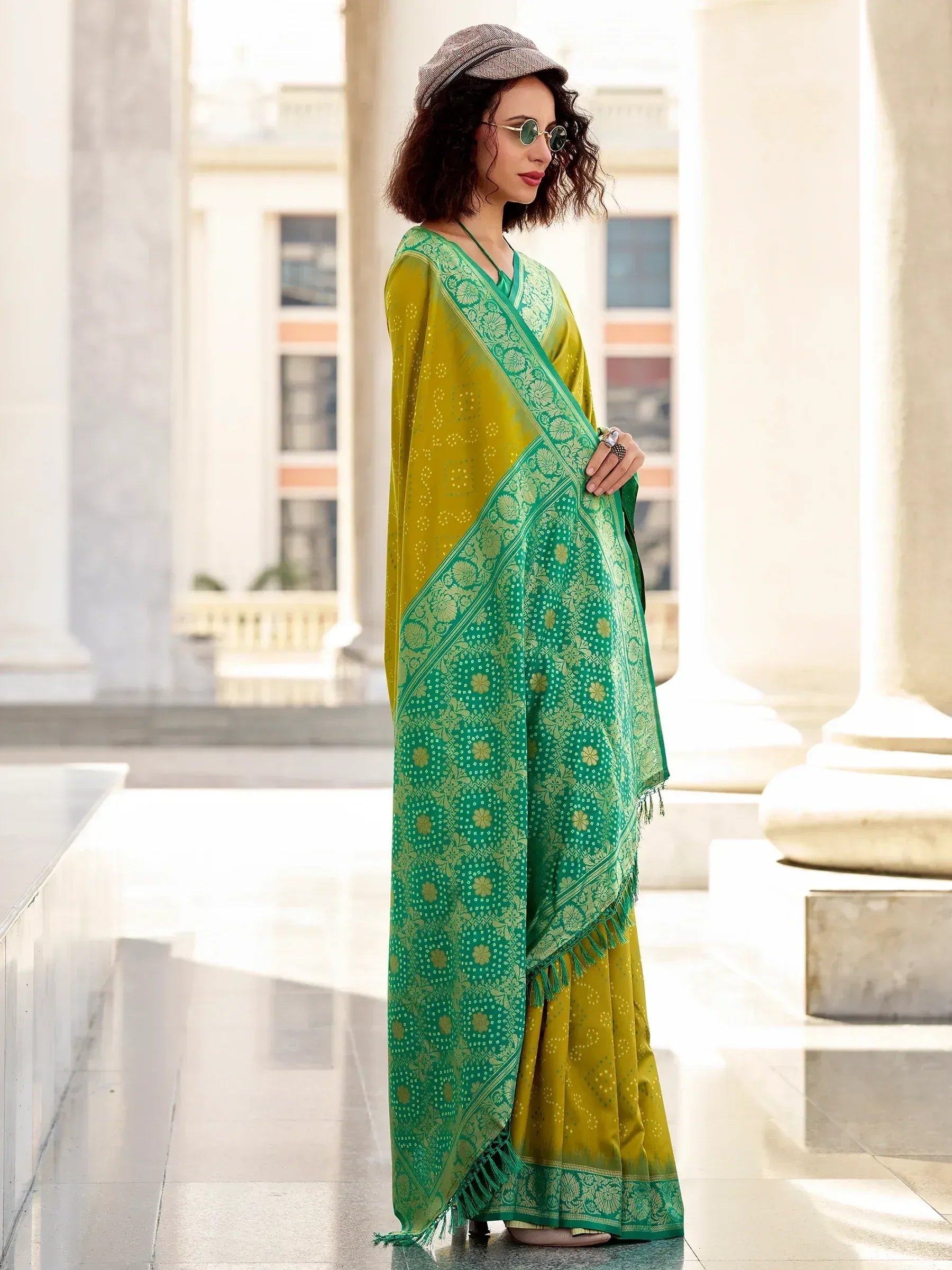 Woman in vibrant green and yellow printed saree with floral border, styled with cap and sunglasses for ethnic fashion.