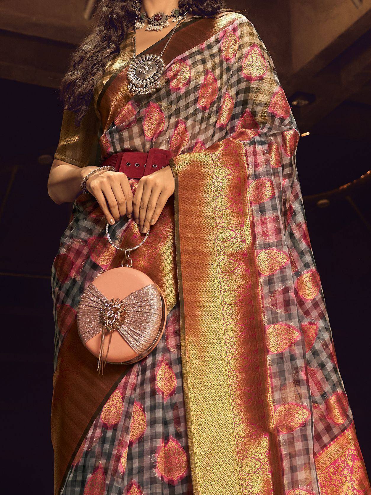 Woman in designer saree with checkered & paisley print, gold border, paired with statement jewelry and round handbag