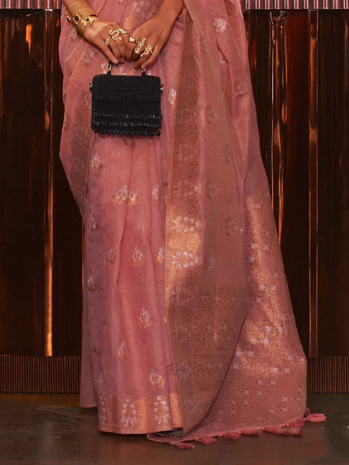 Pink floral saree with gold motifs, paired with black beaded clutch and gold jewelry for ethnic wear