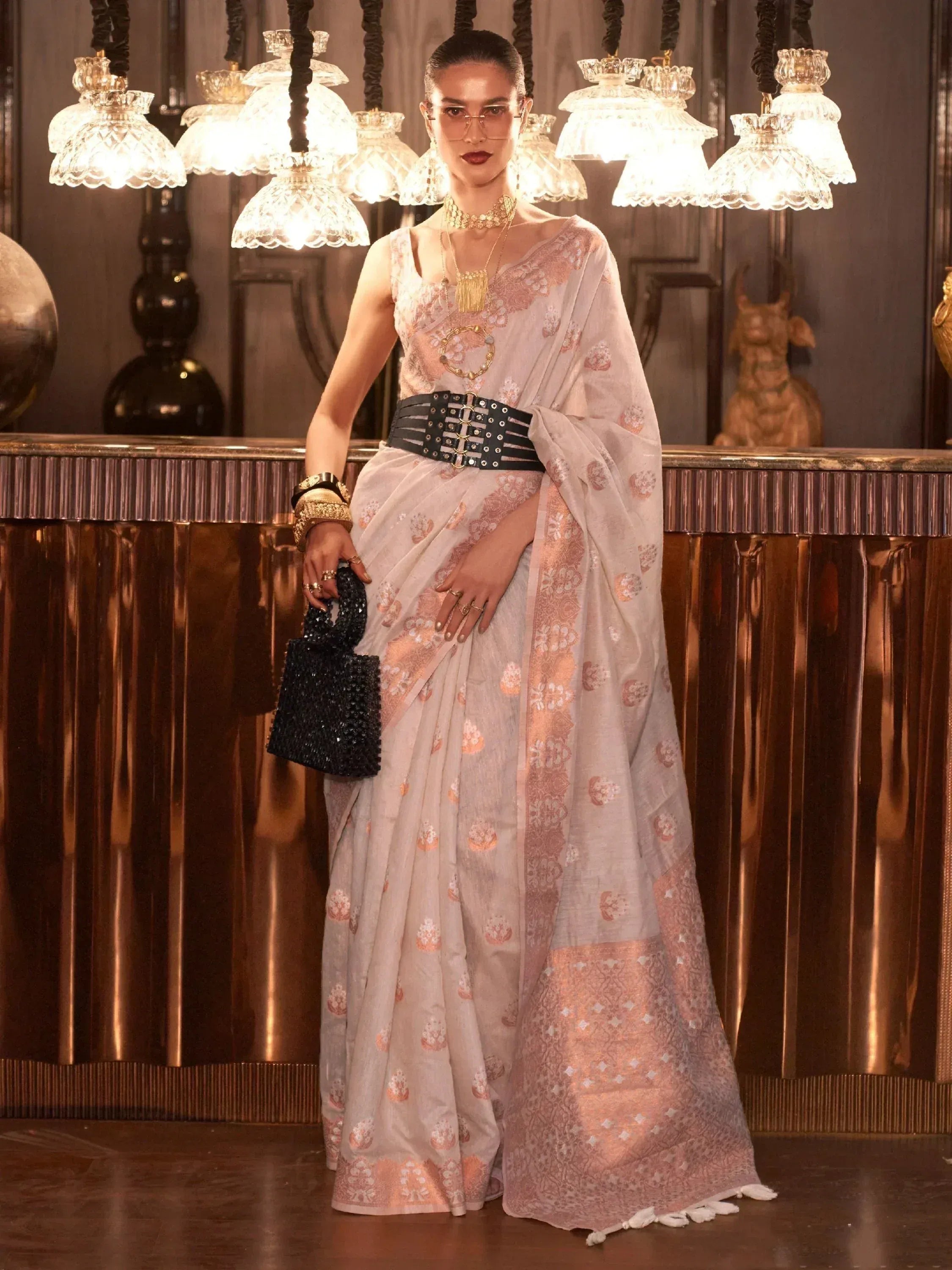 Elegant woman in designer saree with gold embroidery, black belt, and statement jewelry, styled for ethnic fashion.