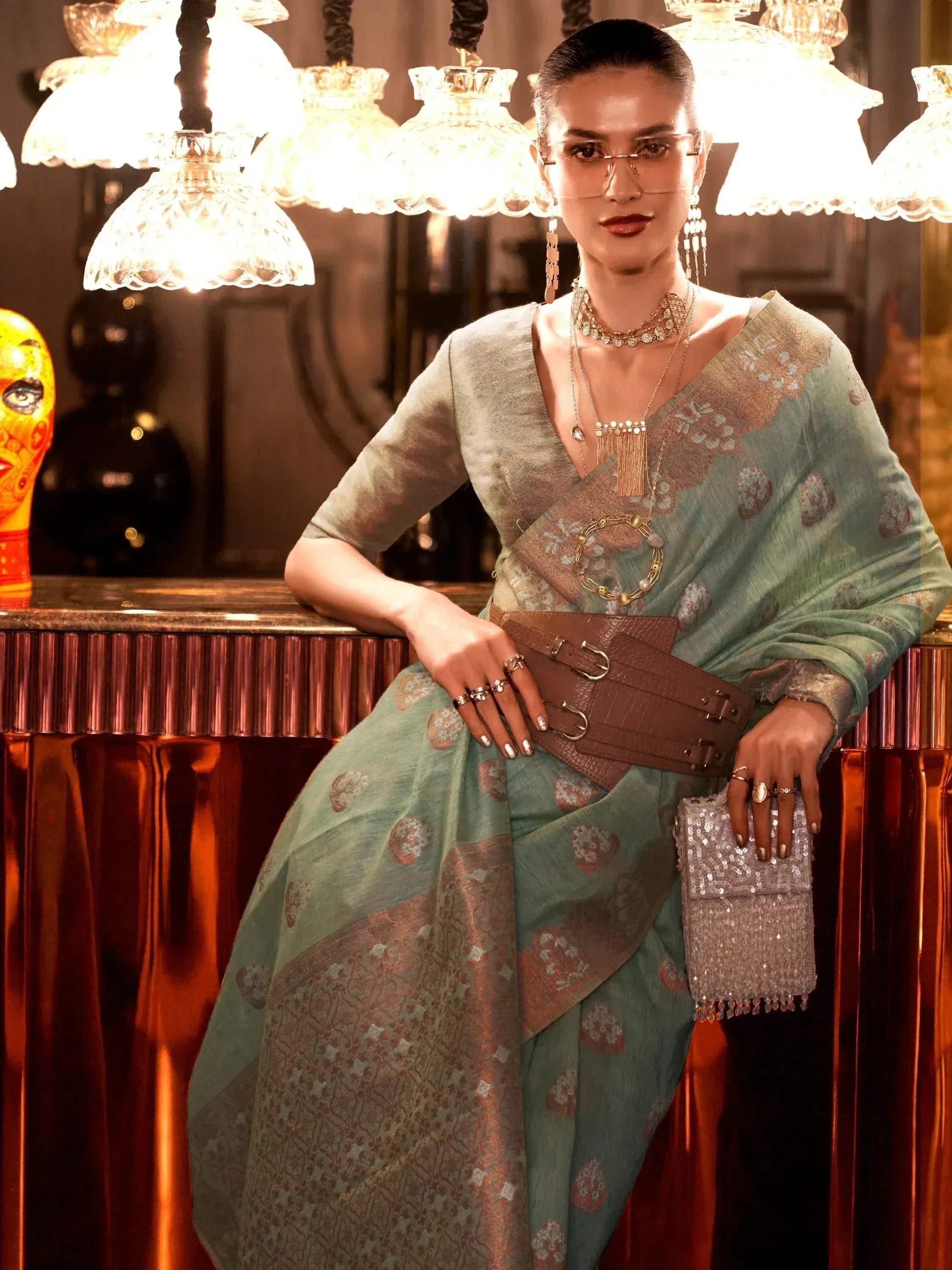 Stylish woman in mint green printed saree with gold embroidery, accessorized with statement jewelry and belt, perfect for Indian ethnic wear.
