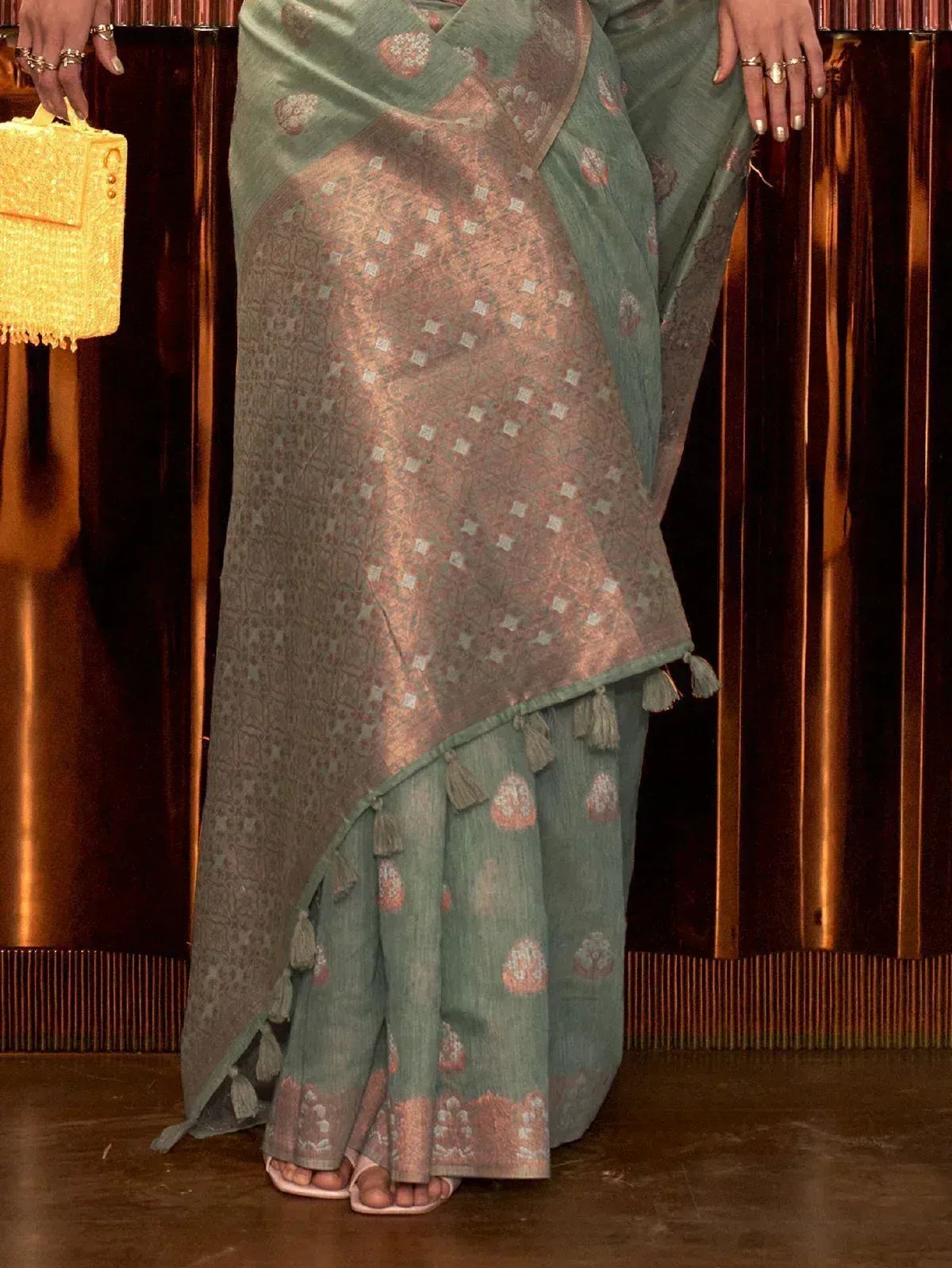 Elegant green saree with gold motifs and tassels, paired with a yellow handbag for ethnic wear.