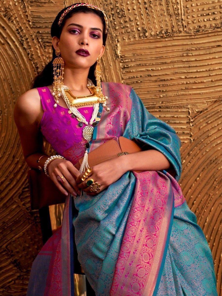 Woman in vibrant pink and teal designer saree with gold jewelry, ethnic wear for festive occasions