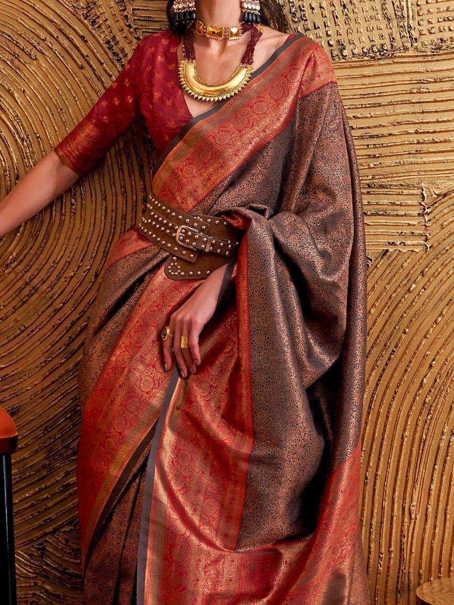 Rich maroon and gold designer saree with intricate patterns, paired with bold gold jewelry and a studded belt.
