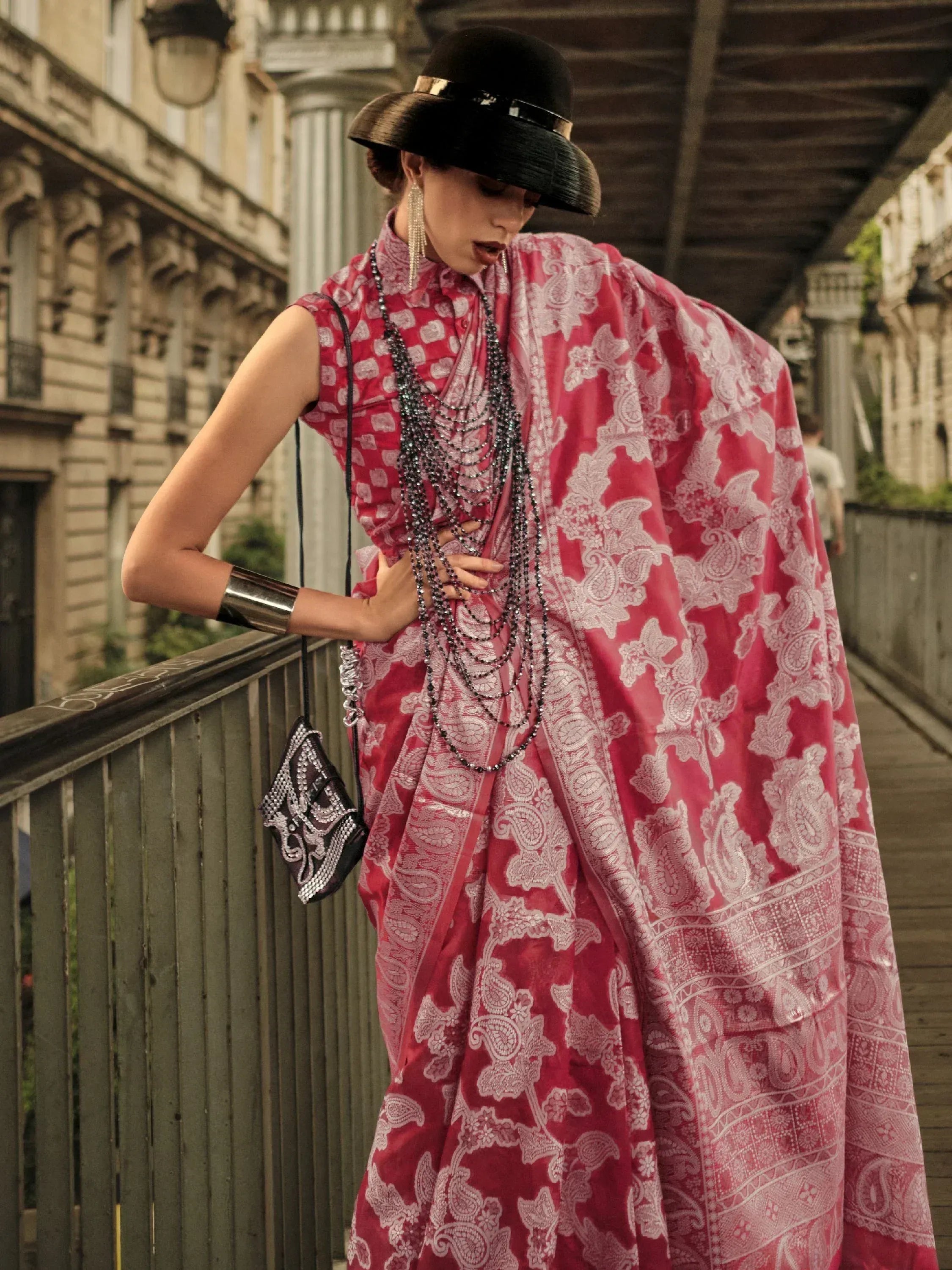 Woman in red paisley saree with black hat and layered necklaces, stylish ethnic wear