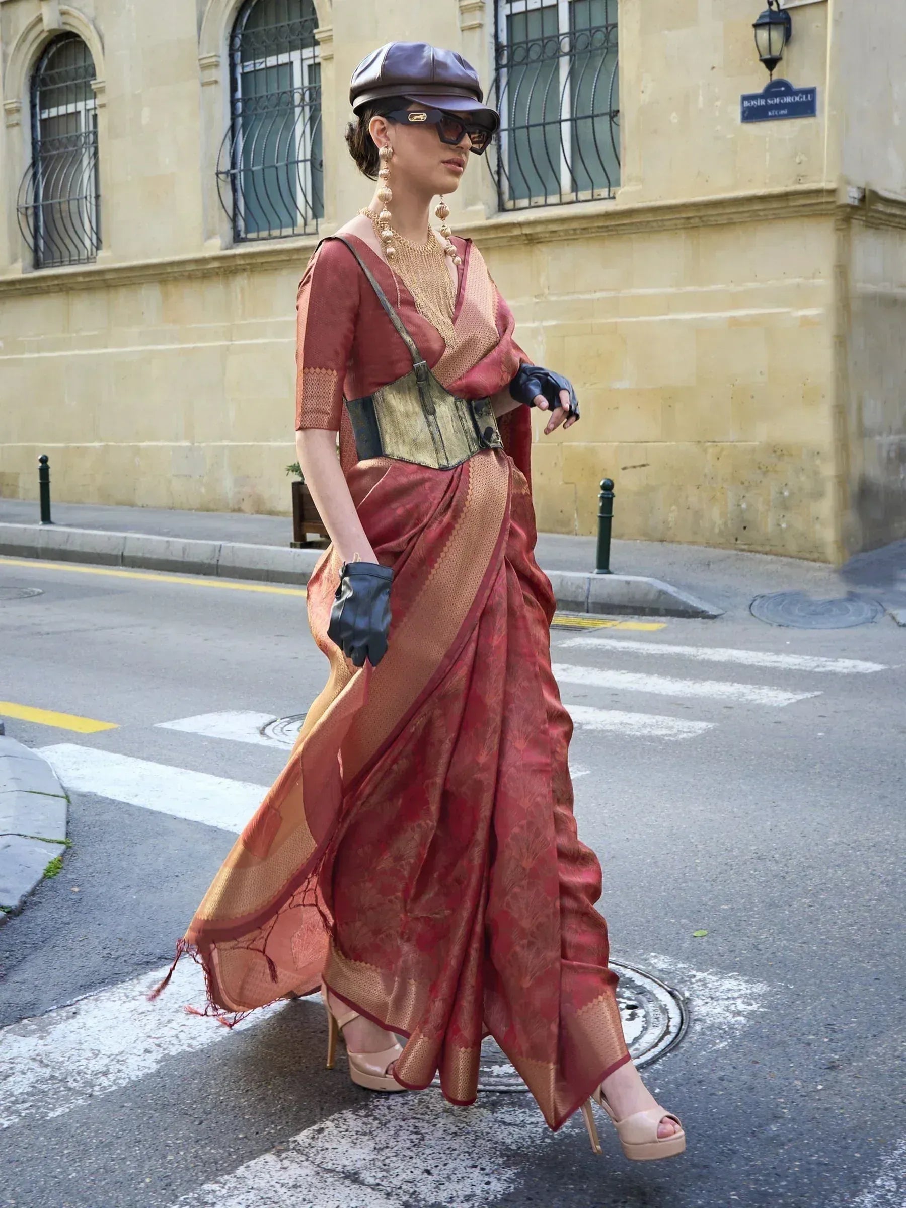 Woman in red and gold designer saree with corset, cap, and gloves walking street