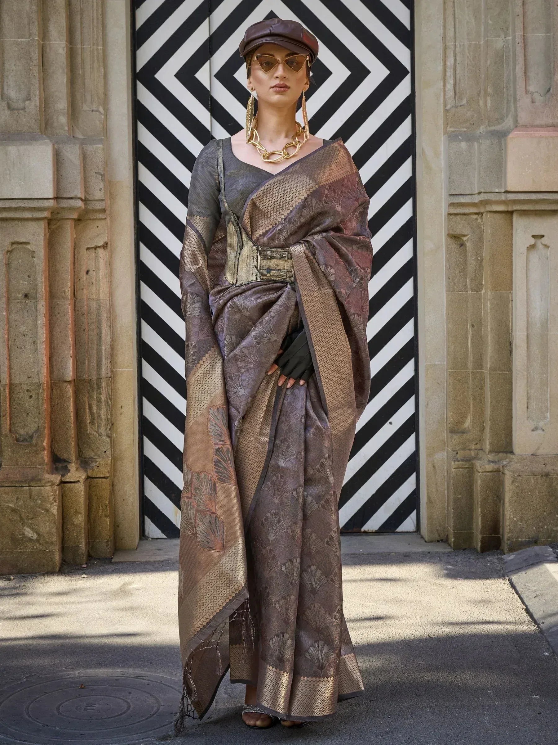 Stylish brown ethnic saree with gold motifs, paired with cap and statement jewelry, modern Indian fashion