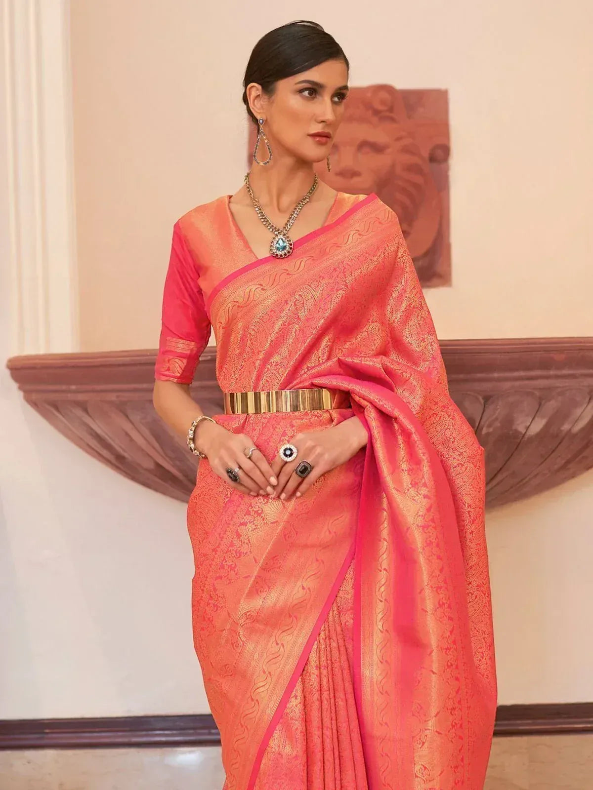 Elegant coral pink designer saree with gold zari work, paired with matching blouse and statement jewelry