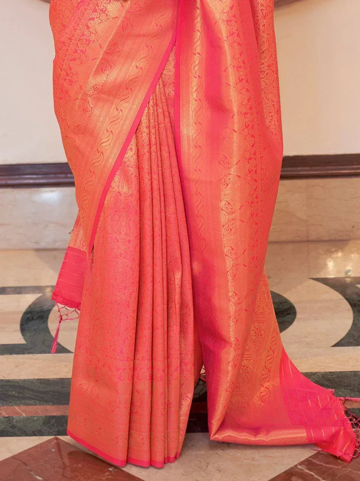 Vibrant coral pink ethnic saree with gold zari paisley patterns and bold border, perfect for Indian occasions.