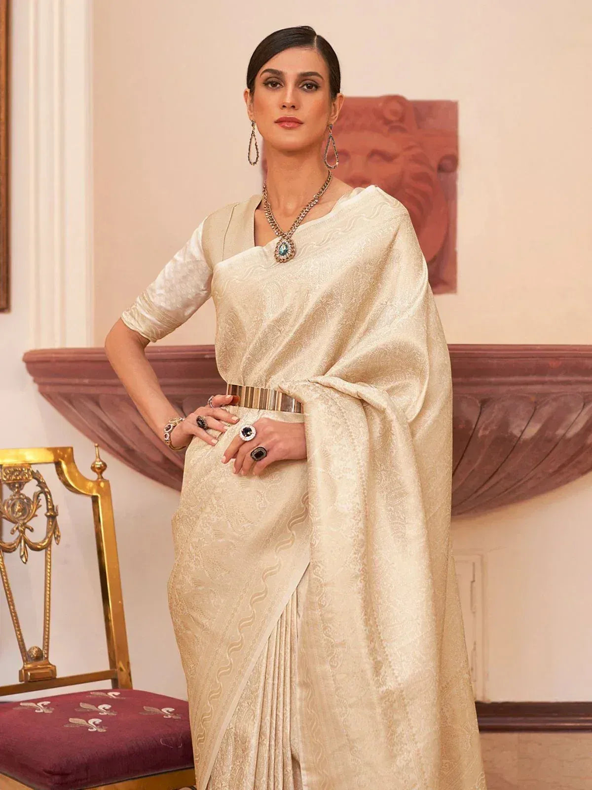 Elegant cream designer saree with intricate patterns, paired with statement jewelry for ethnic wear.
