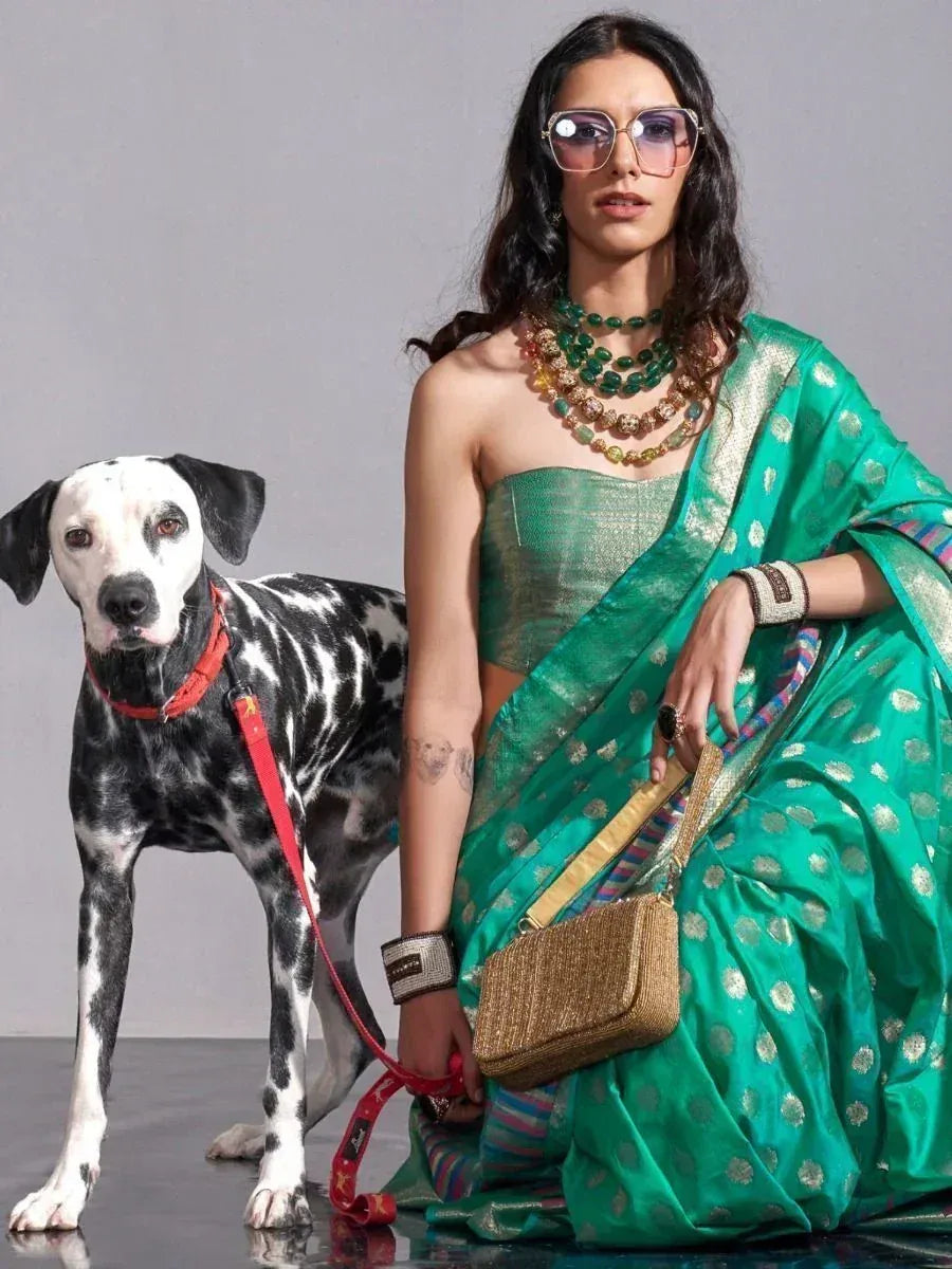 Woman in green designer saree with gold polka dots, holding dog on red leash, styled with statement jewelry and sunglasses