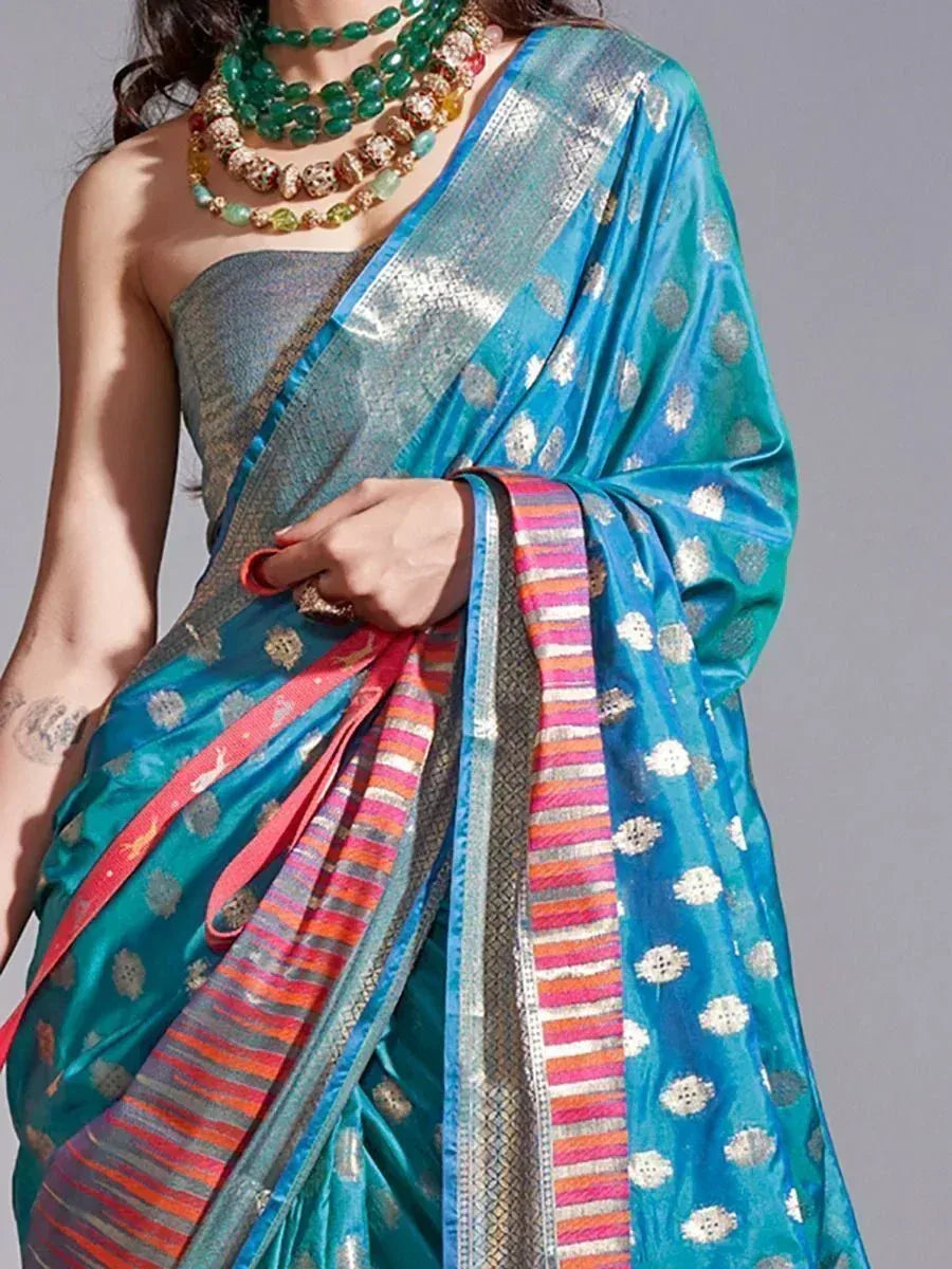 Turquoise designer saree with silver motifs and colorful striped border, paired with statement green necklace