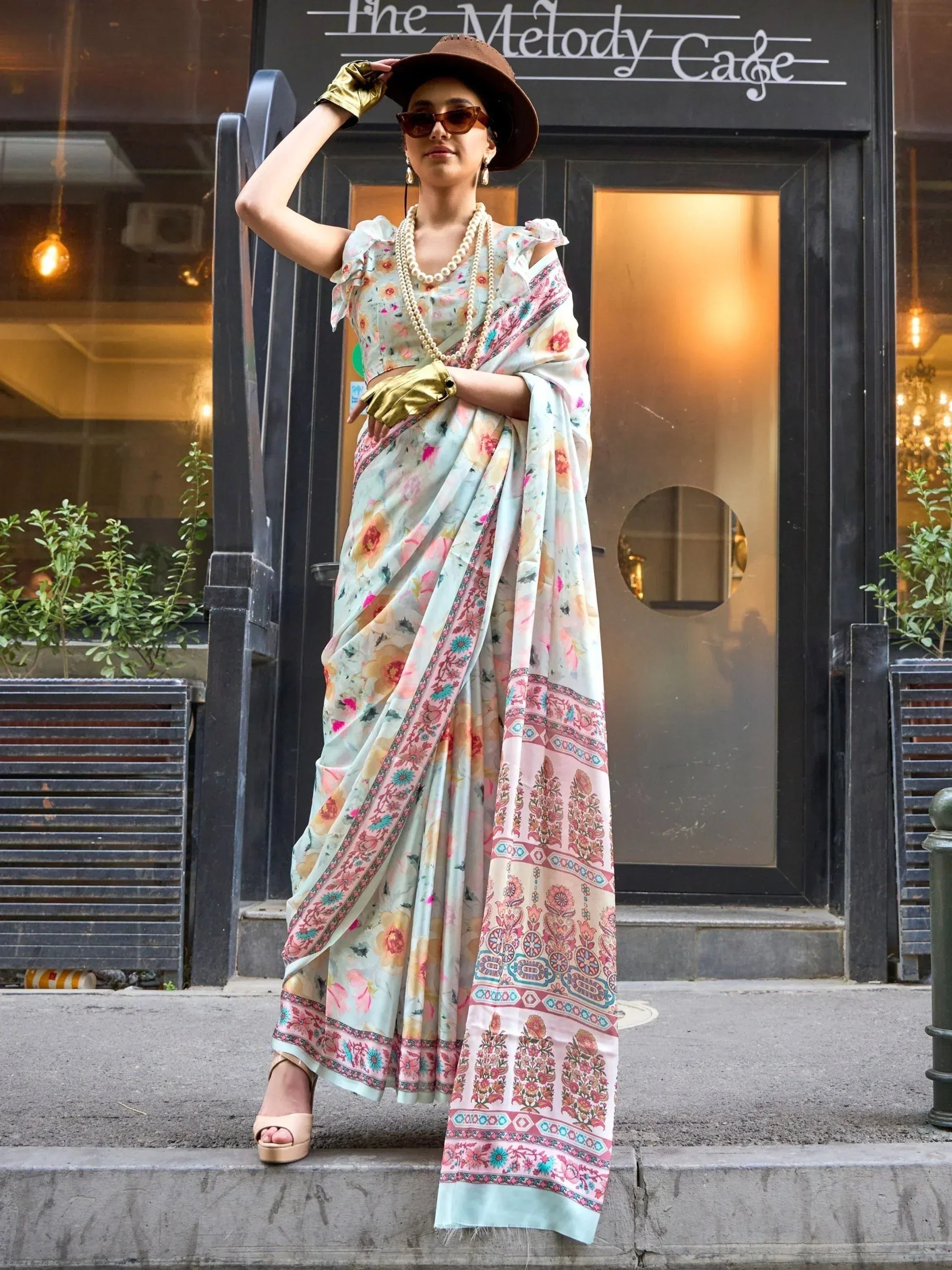 Woman in floral printed saree with ruffle blouse, gold gloves, and hat, styled for ethnic fashion