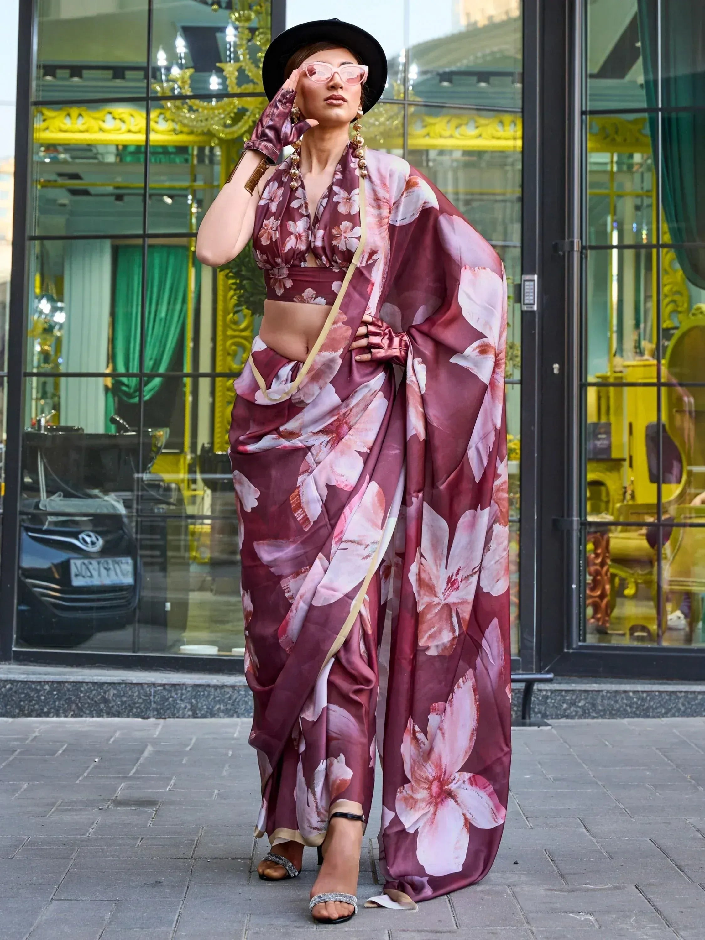 Woman in maroon floral saree with modern blouse, hat, and sunglasses, styled for ethnic fashion.