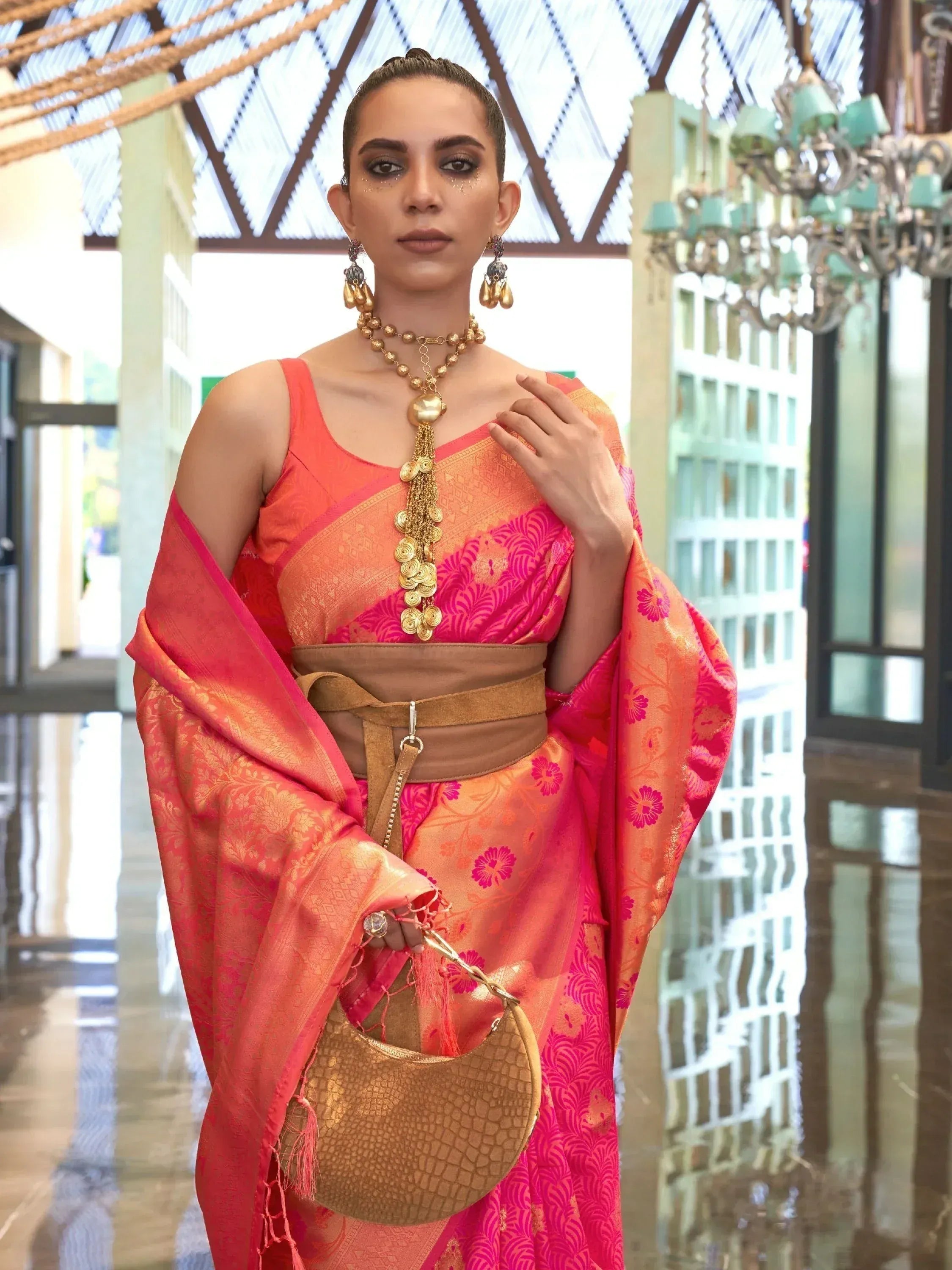 Woman in vibrant pink and orange ethnic saree with gold jewelry and designer handbag