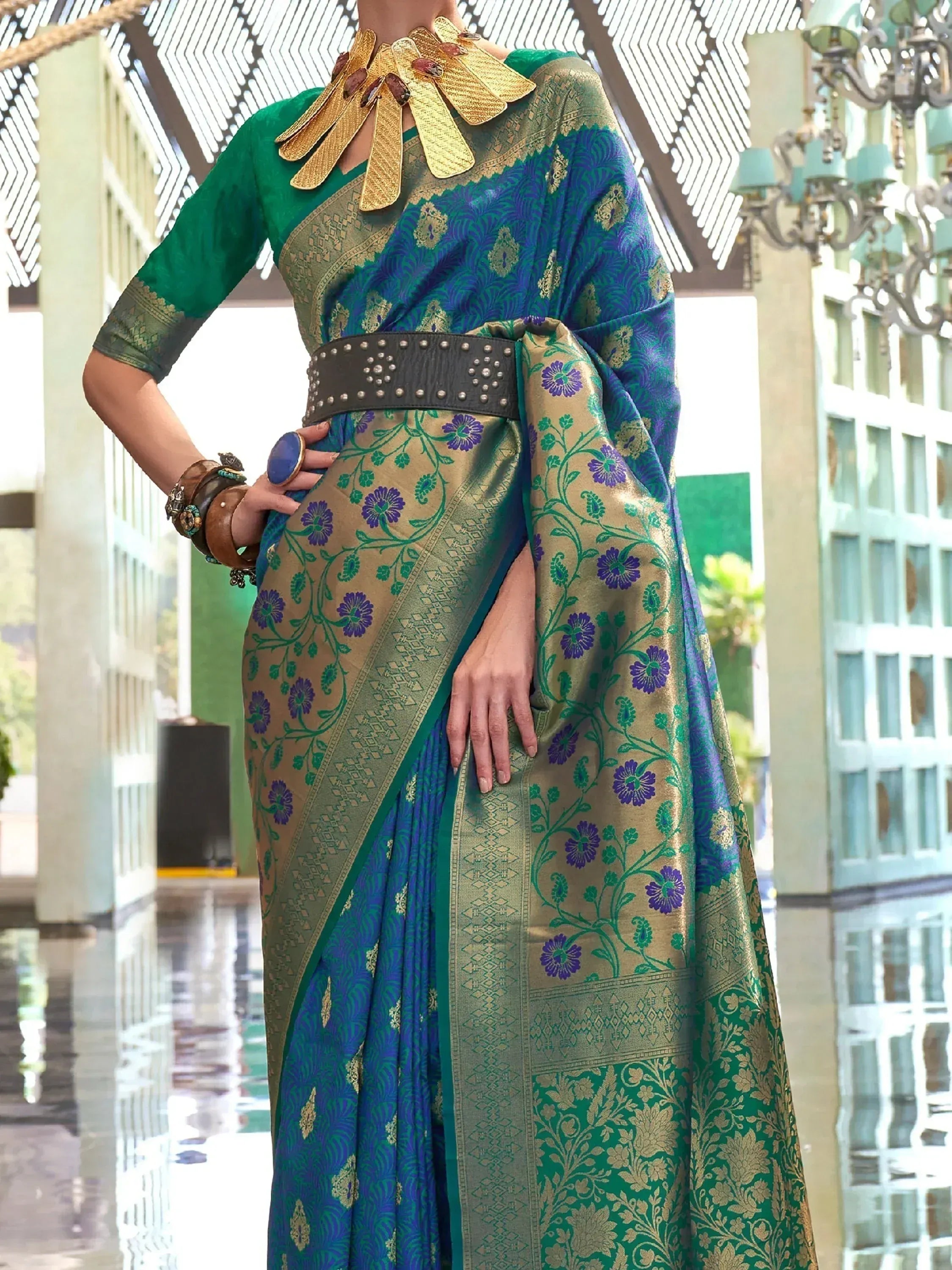 Elegant blue and green floral saree with gold zari, paired with statement gold necklace and studded belt.