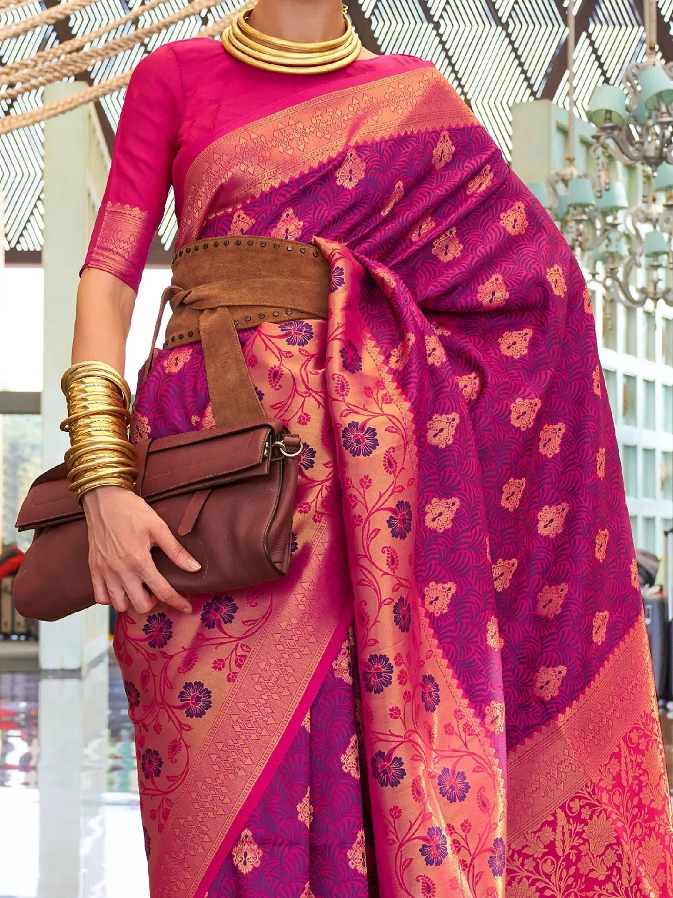 Vibrant pink and gold floral saree with designer blouse, styled with gold jewelry and brown belt bag