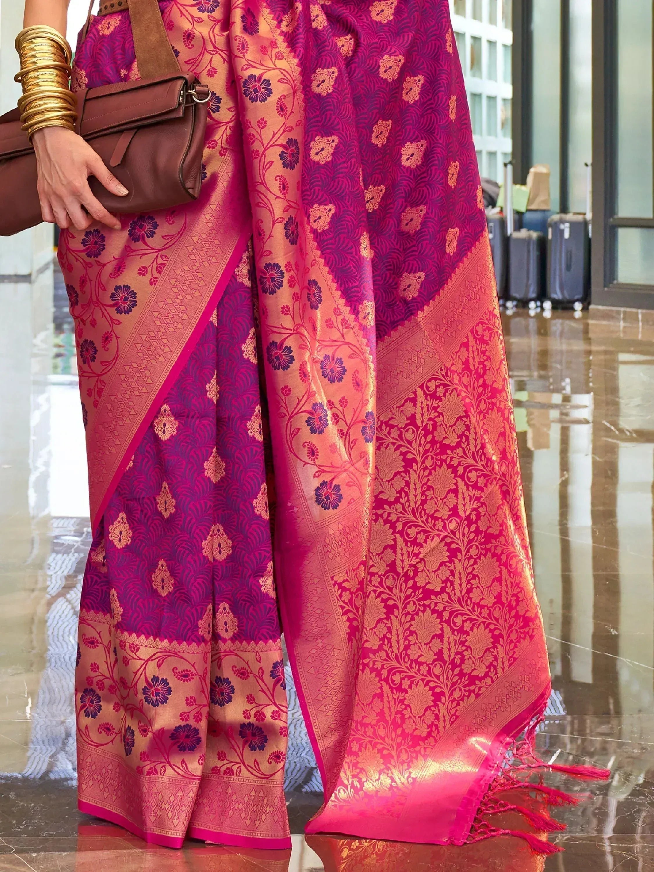 Vibrant pink and purple floral saree with gold zari work, paired with gold bangles and brown handbag