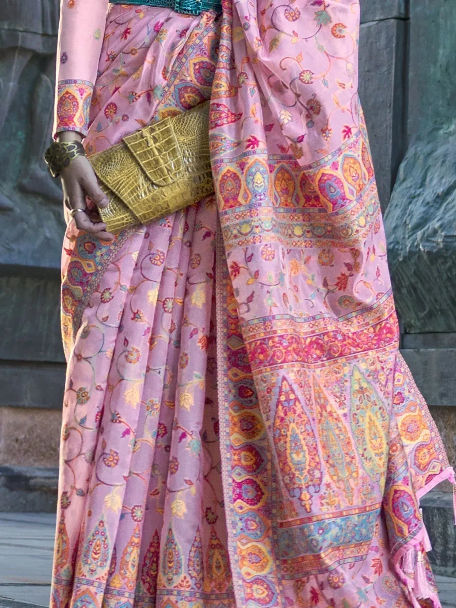Pink floral printed saree with paisley border, paired with gold clutch and bangles, ideal for Indian ethnic wear occasions.