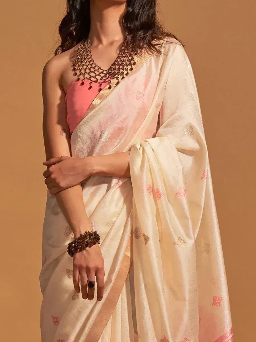 Elegant cream saree with pink motifs, paired with coral blouse and statement jewelry for Indian ethnic wear