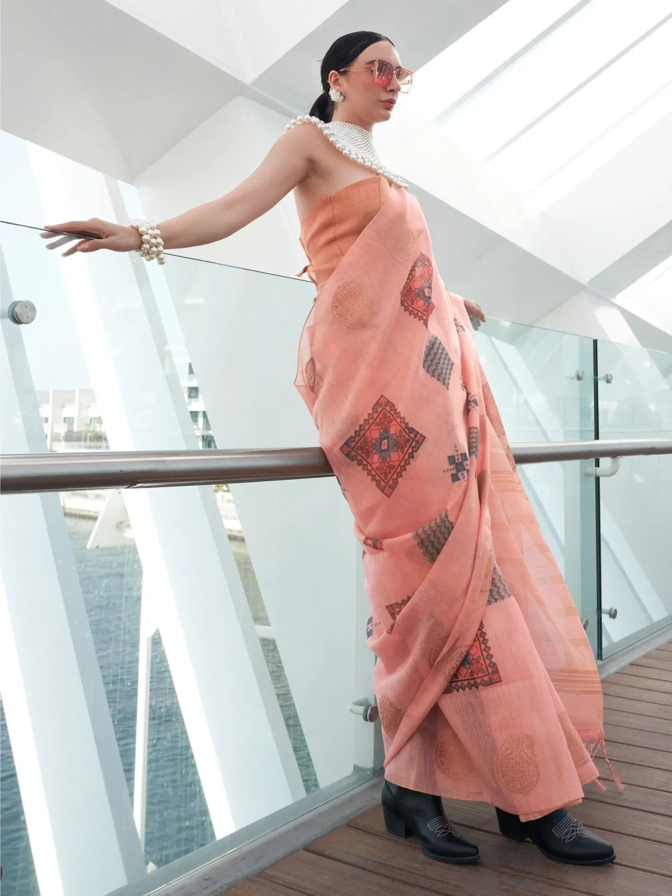 Woman in peach printed saree with pearl accessories, modern ethnic wear for stylish occasions