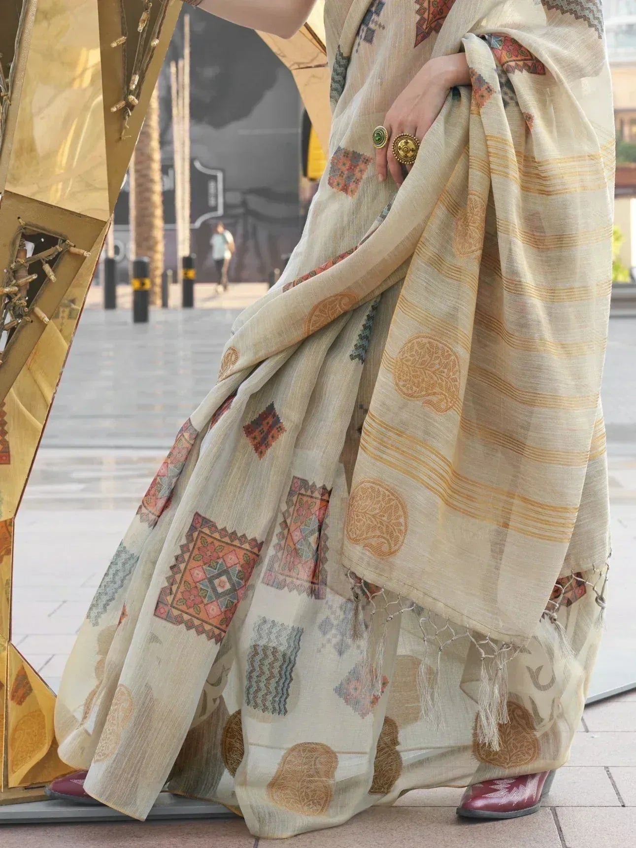 Cream ethnic saree with geometric and tree motifs, tassels, paired with statement rings and burgundy heels