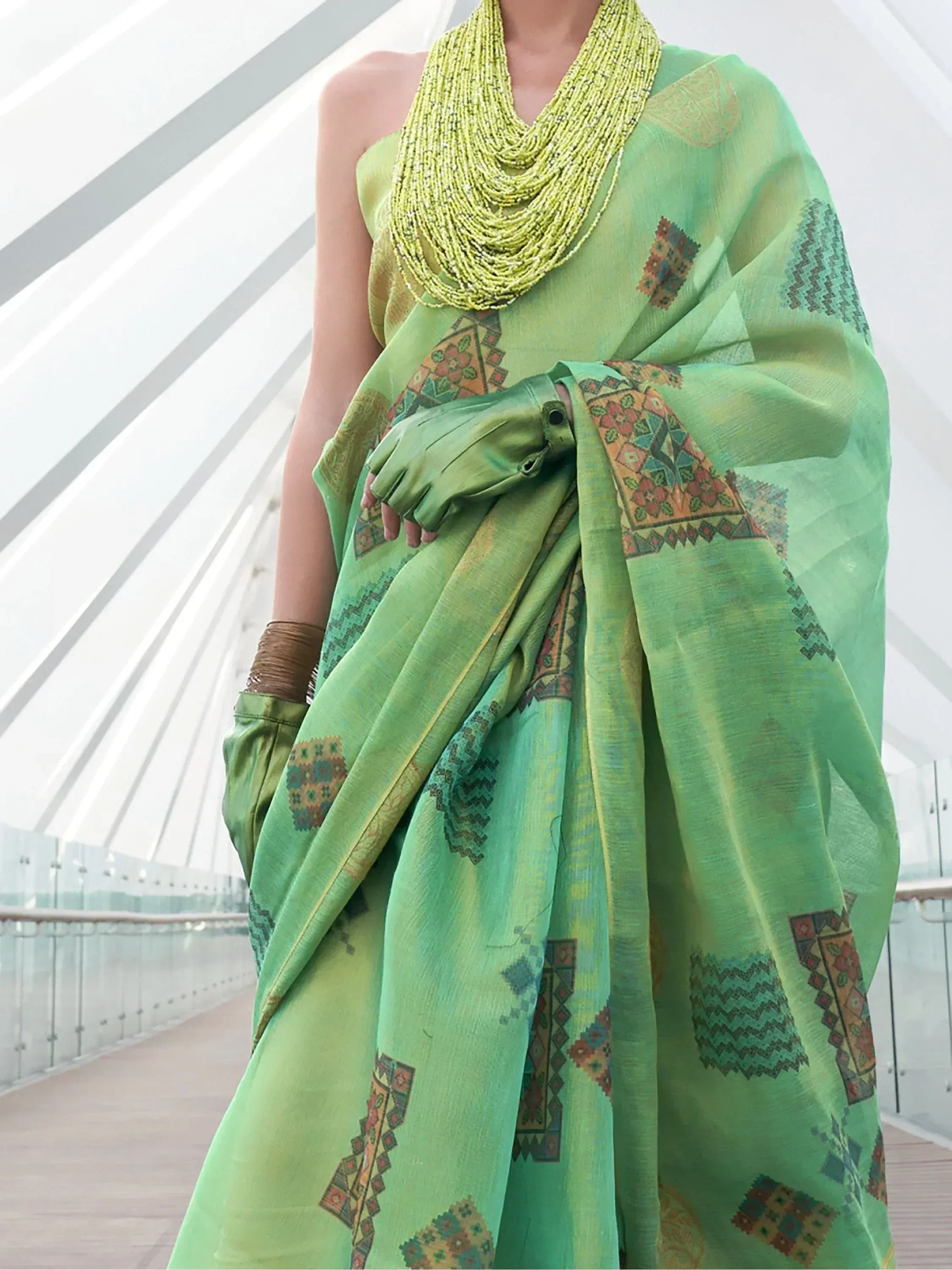 Green ethnic saree with geometric prints, paired with beaded necklace and matching gloves for festive occasions.